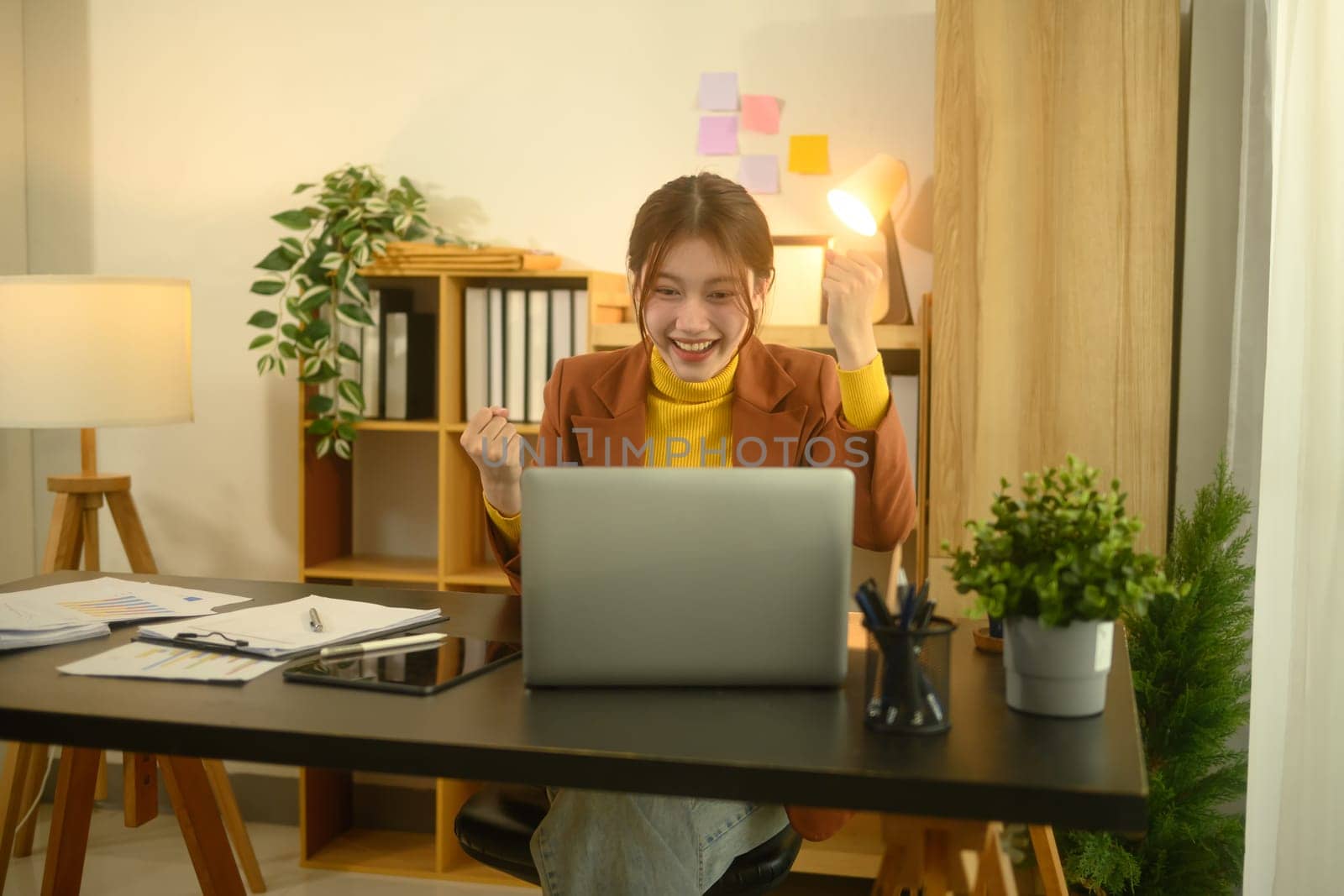 Excited young businesswoman looking at her laptop and celebrating success at work.