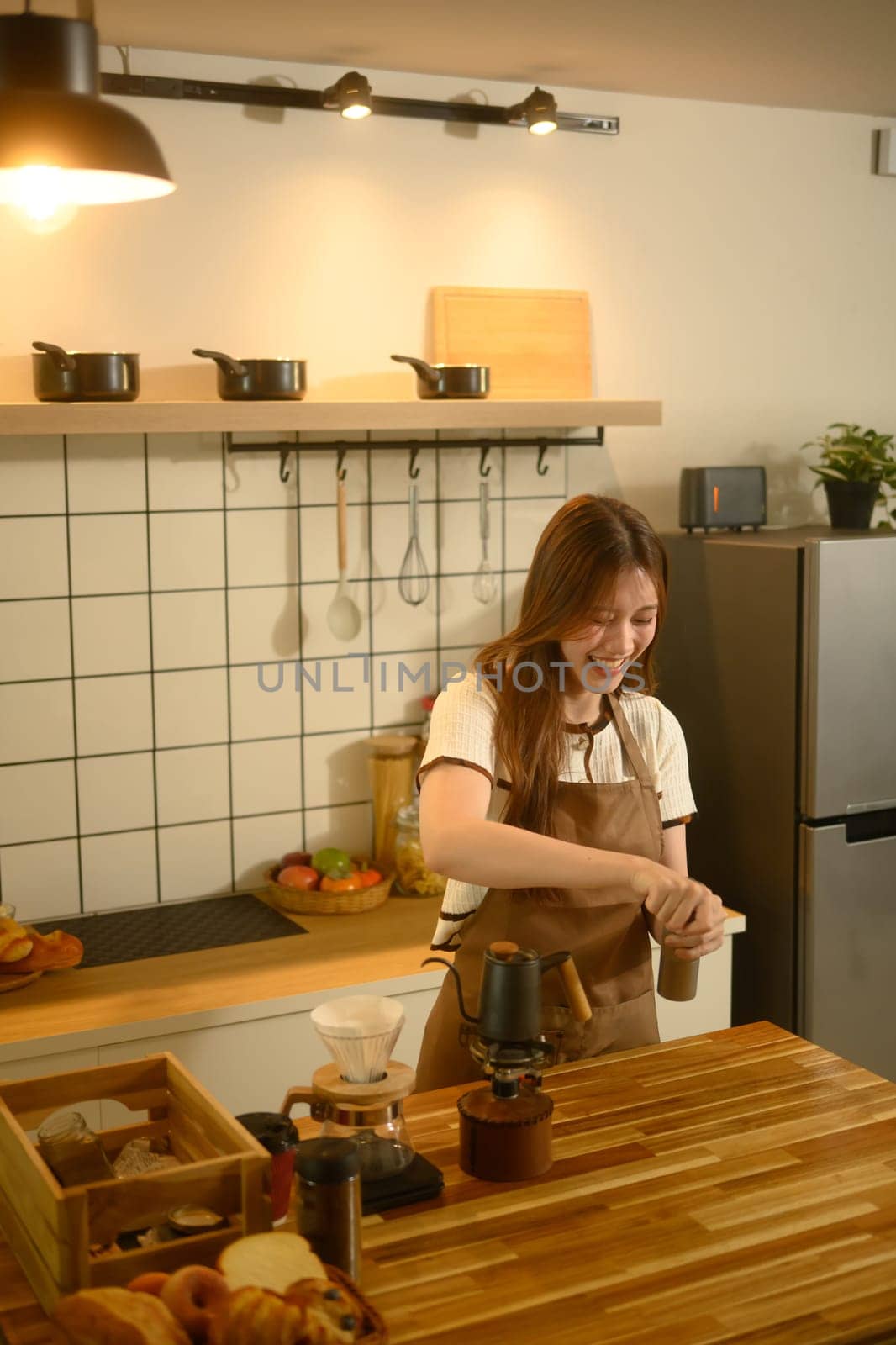 Smiling young woman grinding coffee beans with hand grinder in a kitchen.