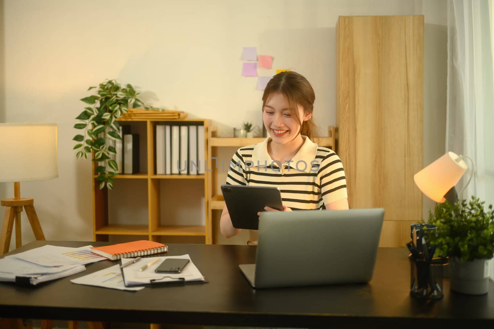 Happy asian female freelancer using digital tablet, working on a digital project at home Office.