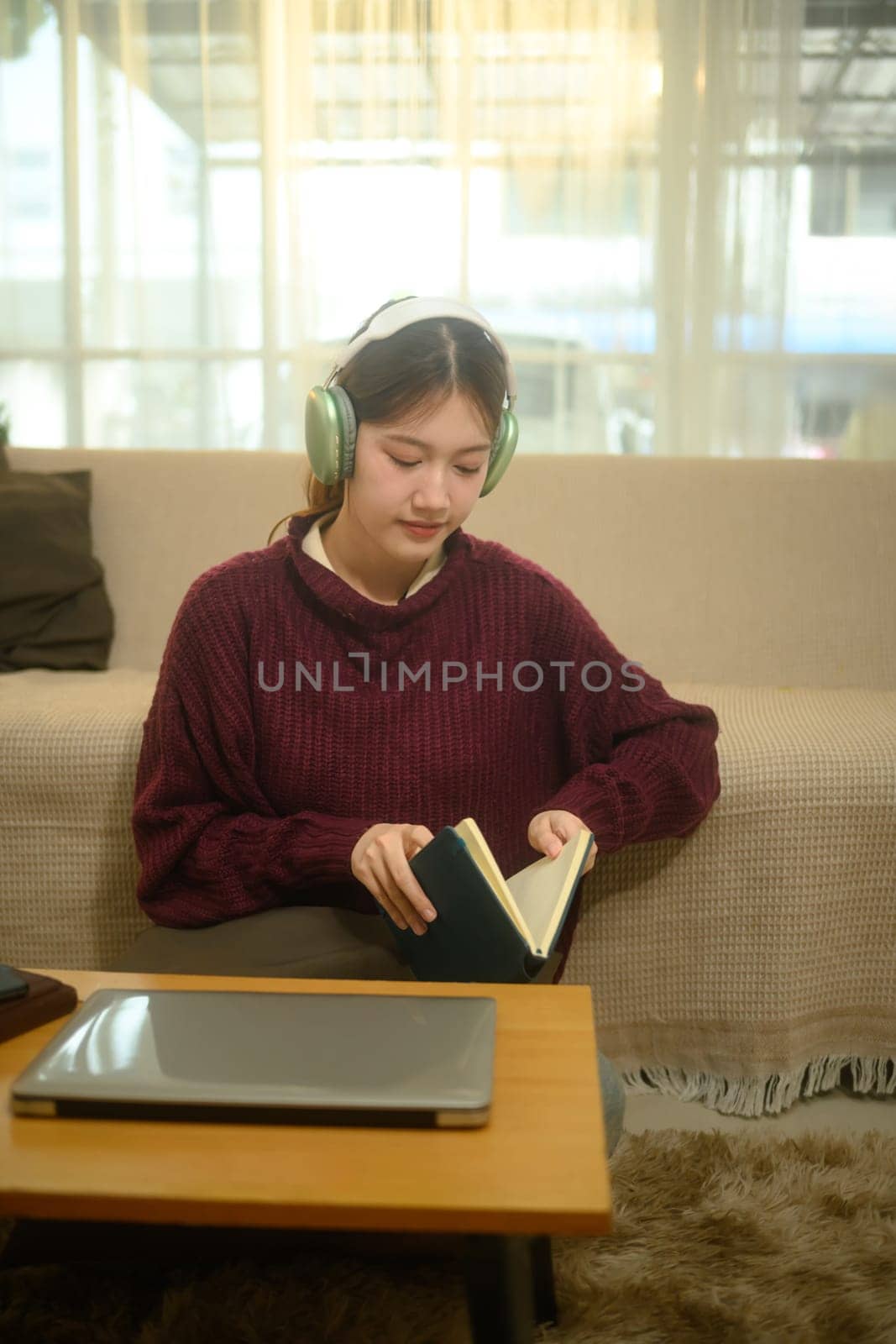 Happy young woman listening to music in headphone and reading book at home.