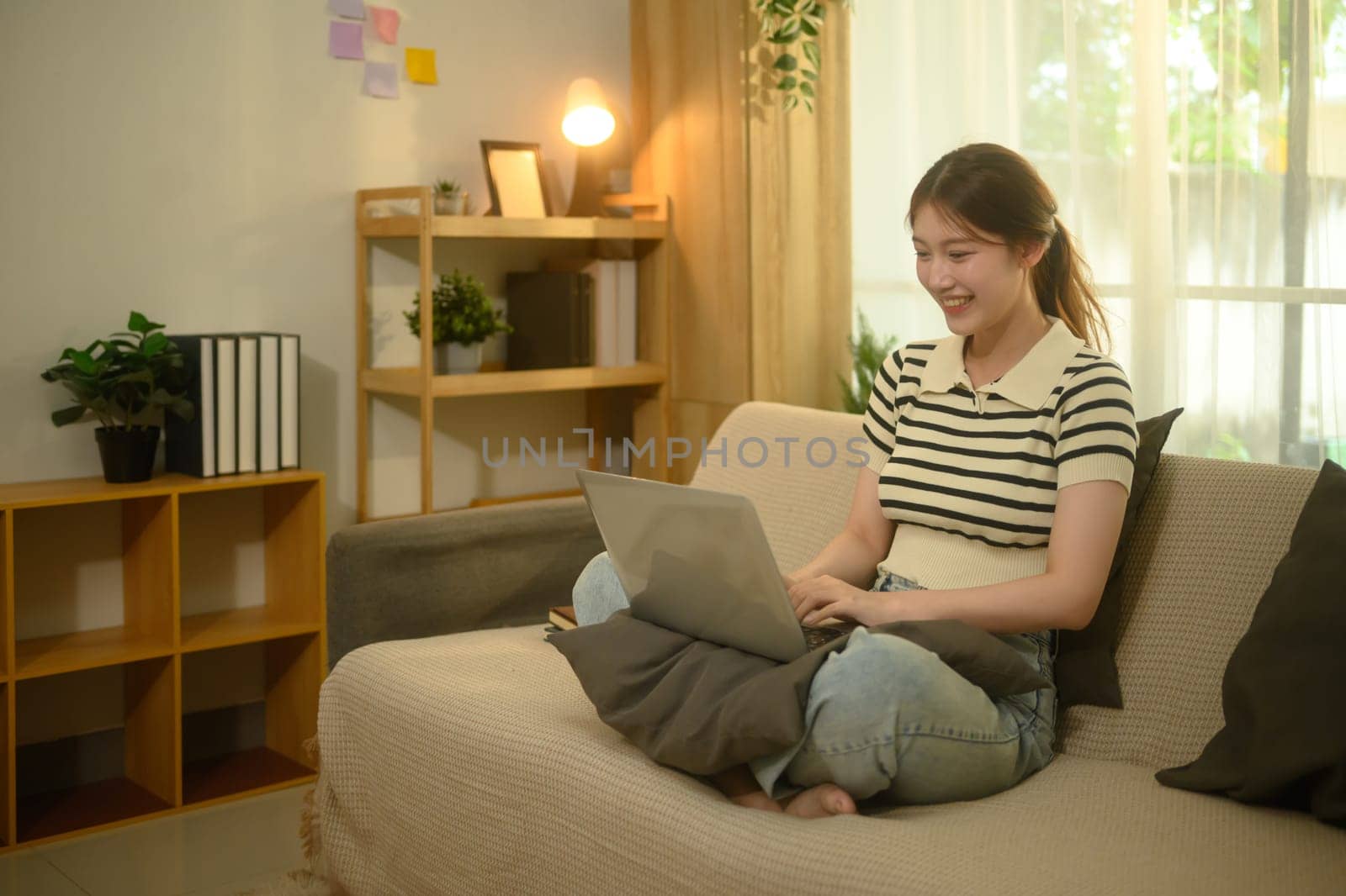 Cheerful young woman sitting on a couch working on her laptop.