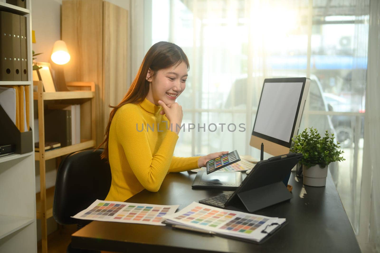 Smiling woman working in a bright office, selecting color palettes for a design project.