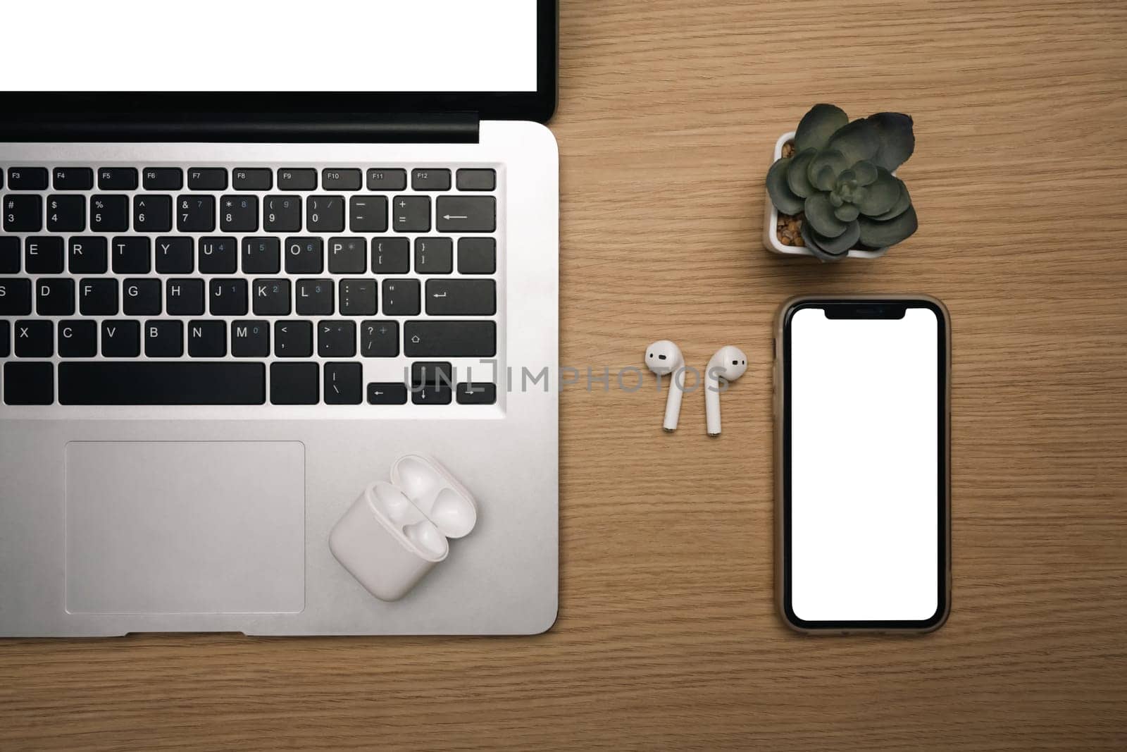 Top view of smartphone with blank screen, laptop and wireless earbuds wooden desk.