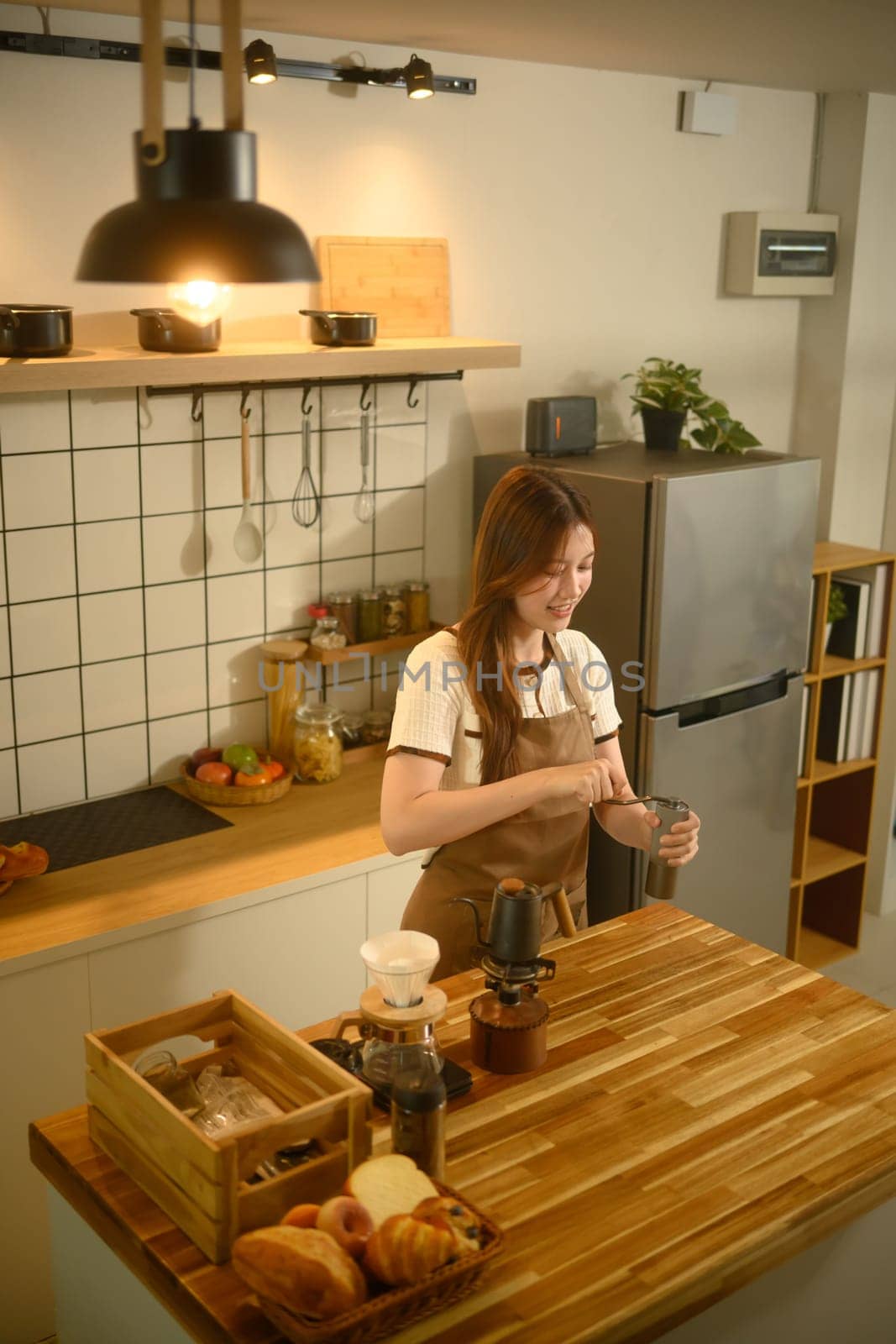 Smiling young woman grinding coffee beans with hand grinder in a kitchen.