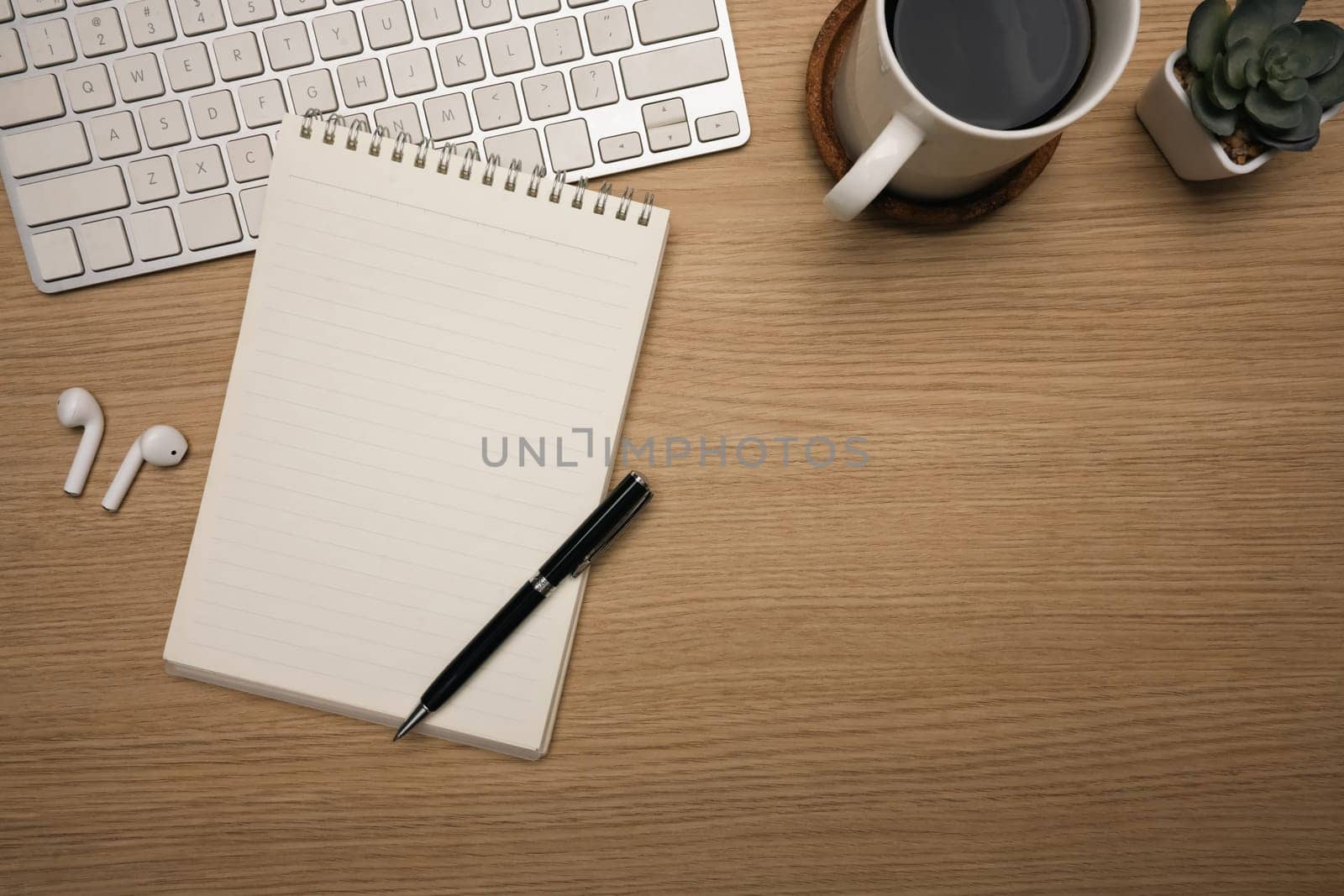 Minimalist workspace with notebook and coffee cup and wireless earbuds on wooden desk.