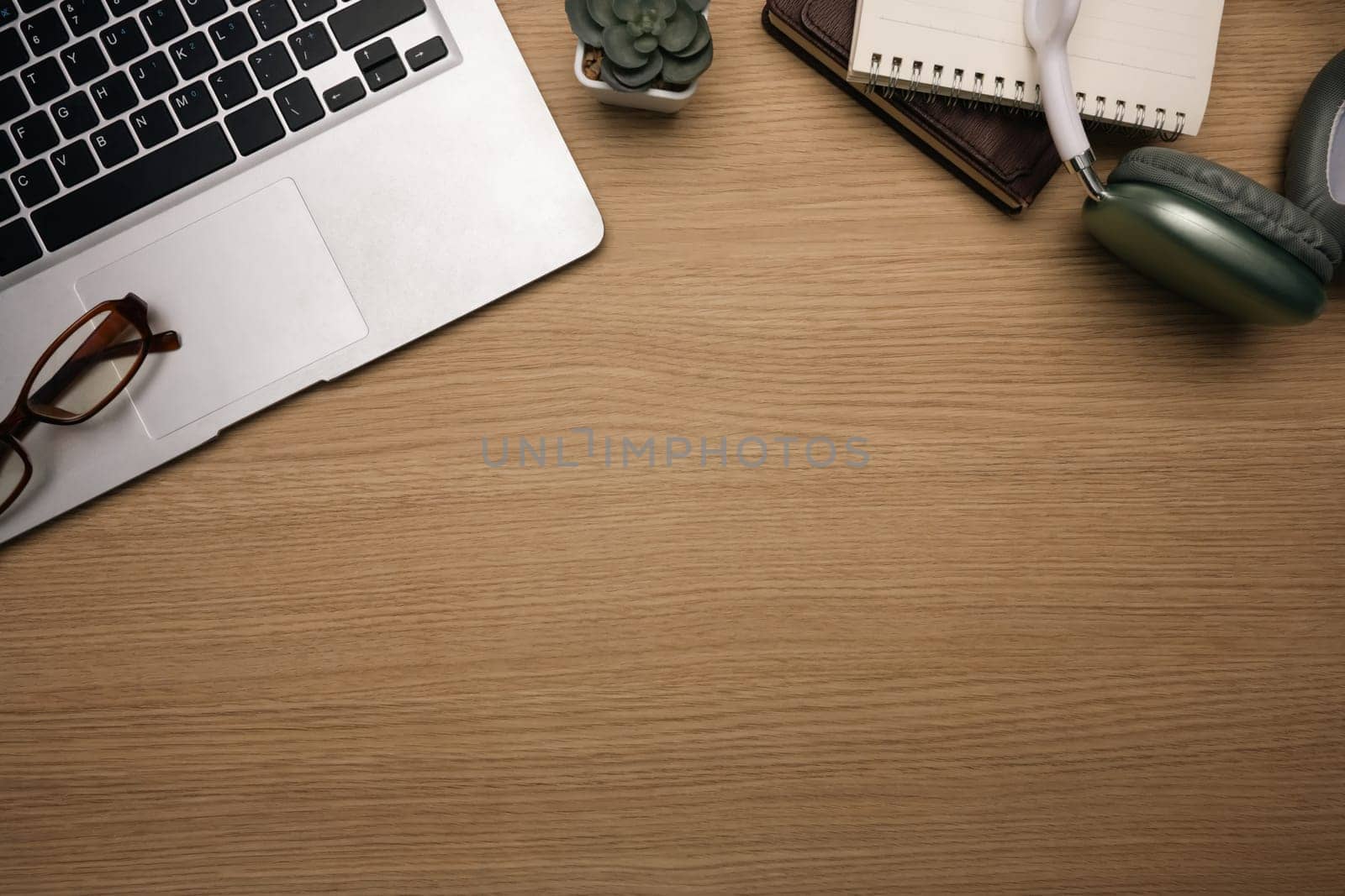 Top view shot of laptop, eyeglasses, notebook and headphones on a wooden desk.