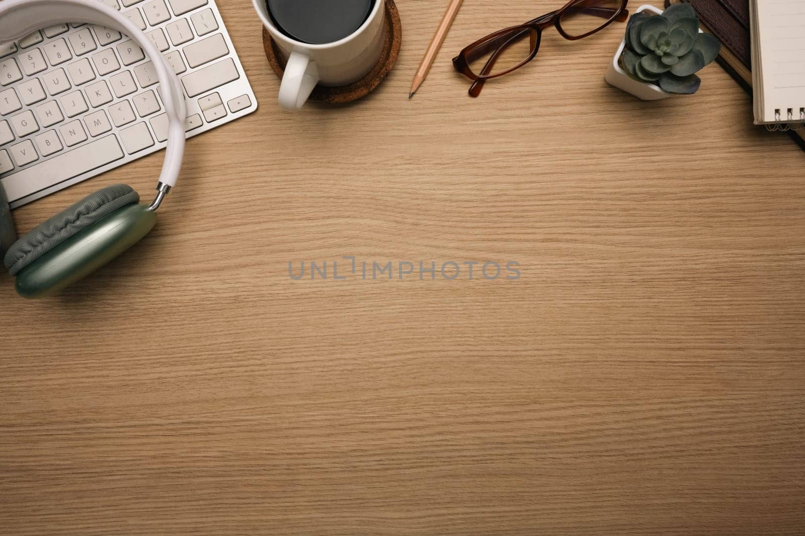 Top view shot of wooden desk with headphone, keyboard, a cup of coffee and eyeglasses.