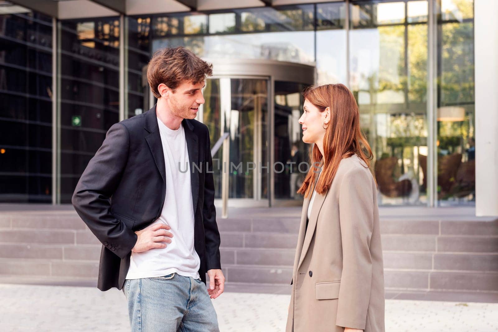 business man and woman standing outside of an office building talking to each other, they are wearing casual clothes