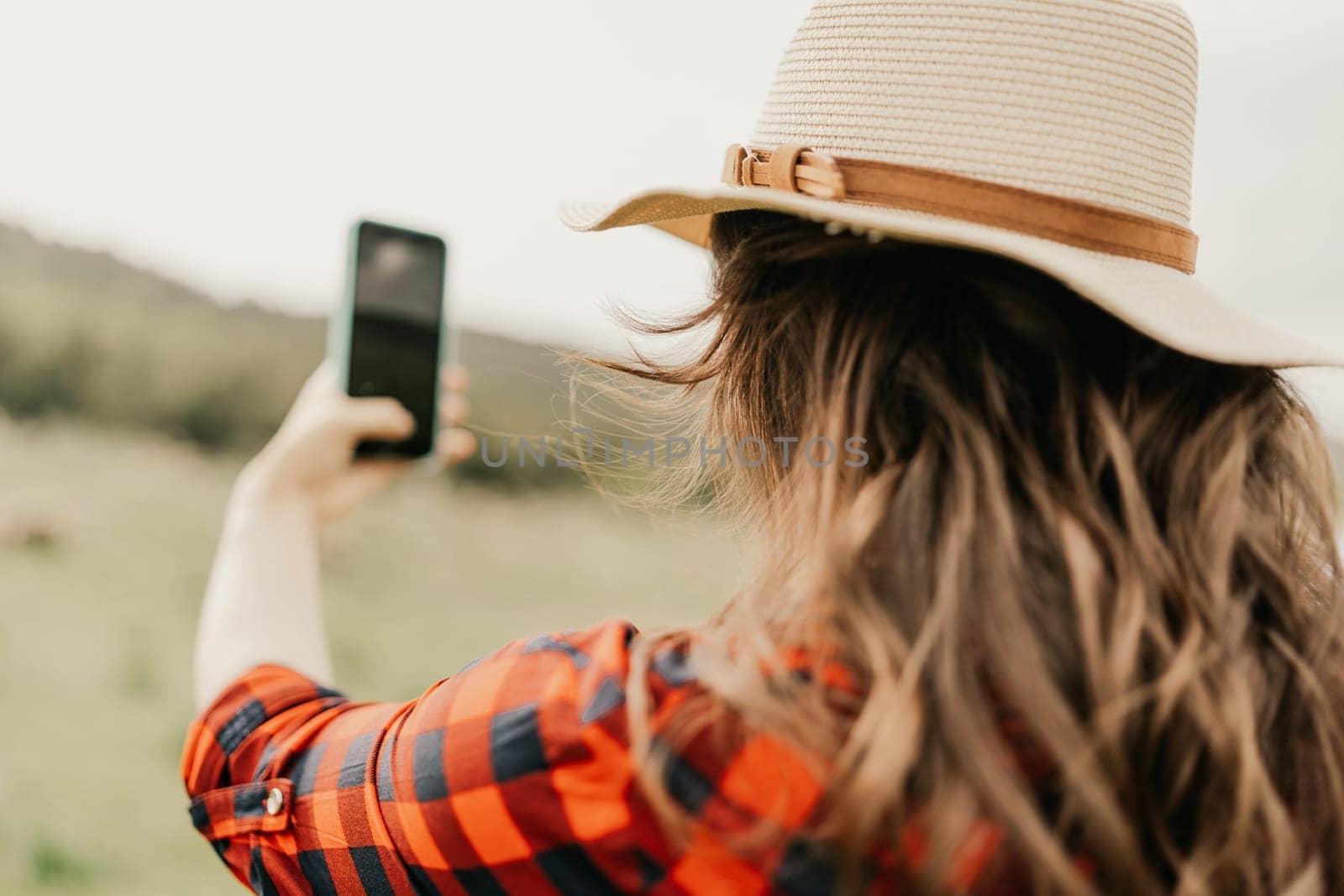 A woman is taking a picture of herself with a cell phone while wearing a straw hat. Concept of leisure and relaxation, as the woman is enjoying her time outdoors