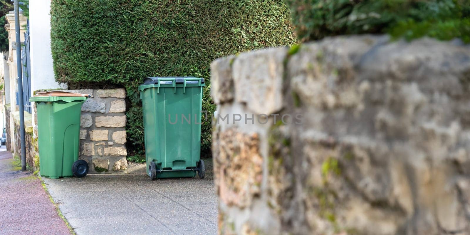 Different colored waste bins are neatly arranged along the side of a residential street. These containers include black, green, blue, and yellow bins for recycling and waste disposal.