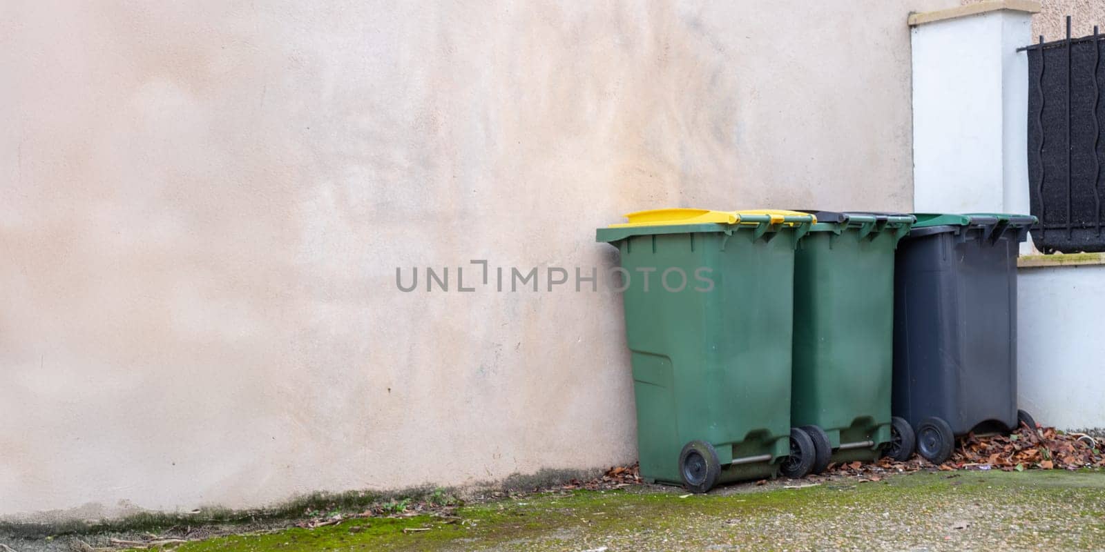 Different colored waste bins are neatly arranged along the side of a residential street. These containers include black, green, blue, and yellow bins for recycling and waste disposal.