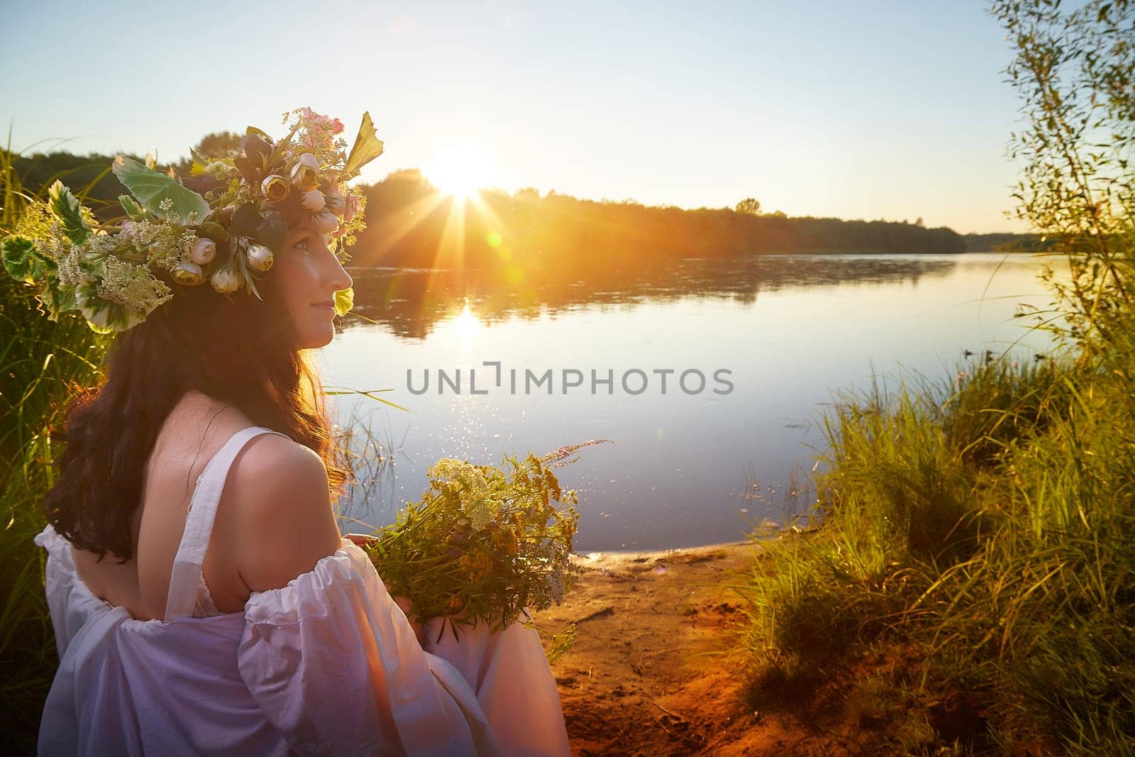 Slavic plump chubby girl in long white dress on the feast of Ivan Kupala with flowers and water in a river or lake on summer evening