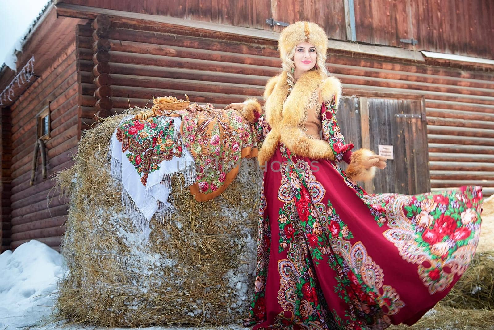 Celebrating Maslenitsa, a lovely Russian girl in vibrant national attire poses gracefully with a horse in winter.