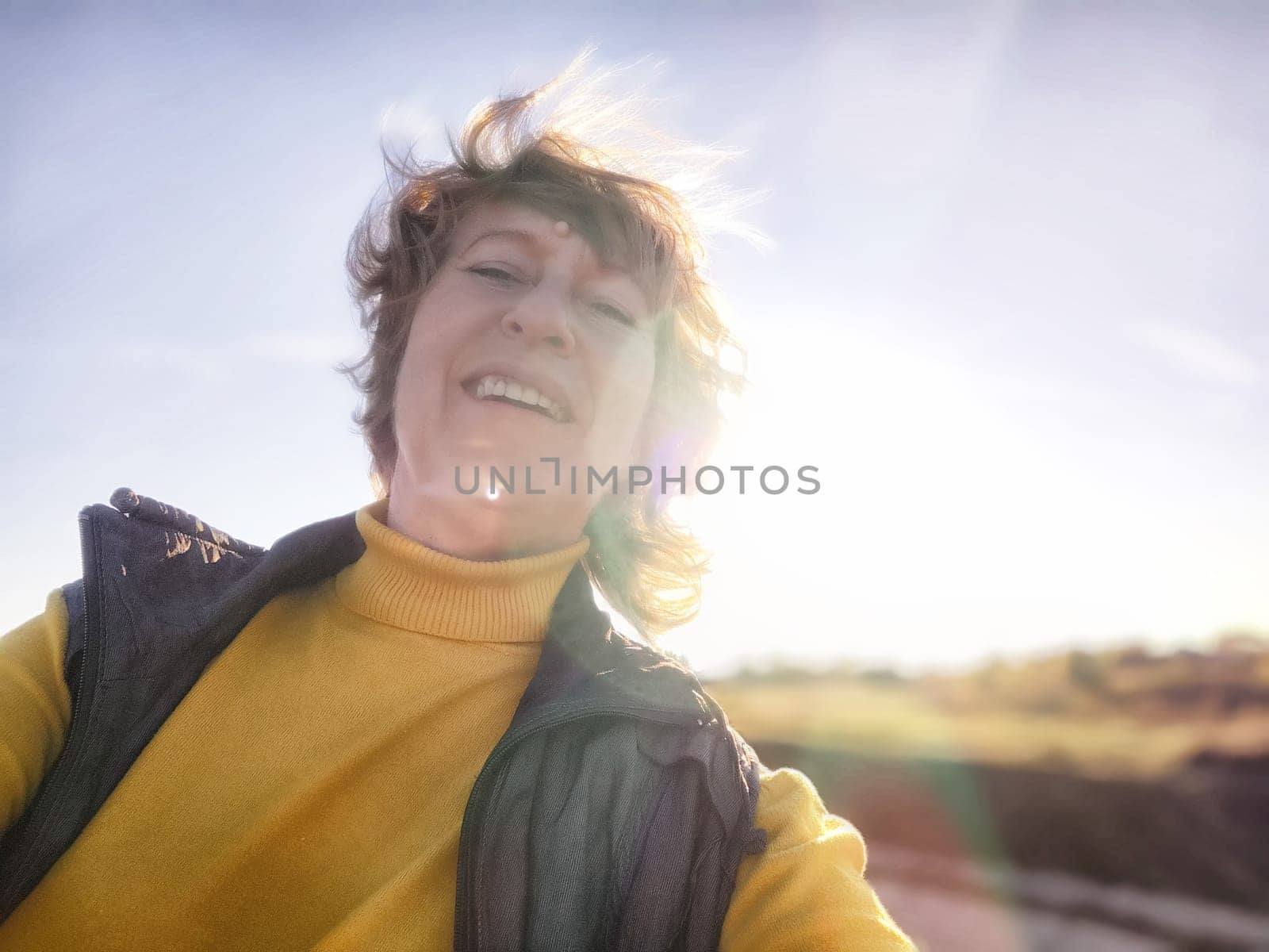 A blonde woman happily captures a selfie during her travel excursion, embracing the warm sunlight and scenic background.