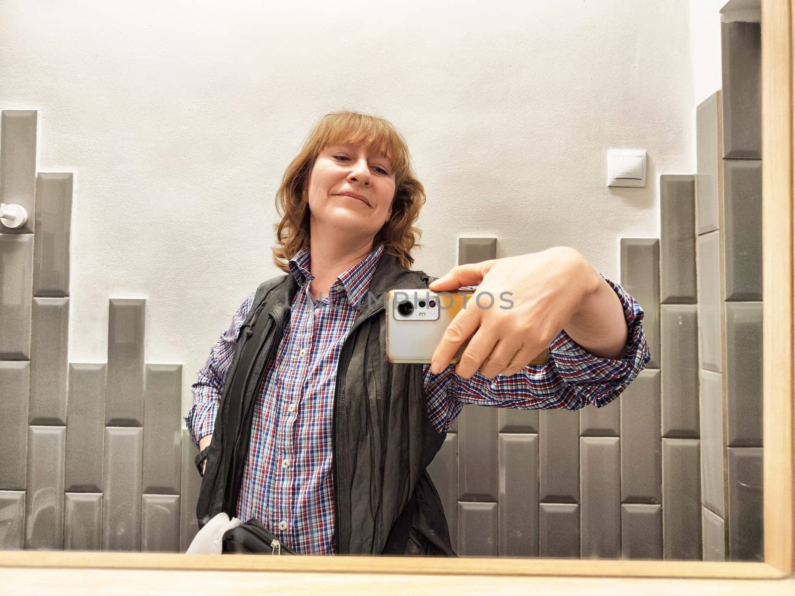 A middle-aged female blogger enjoys a cheerful moment as she takes a selfie in the bathroom early in the morning.