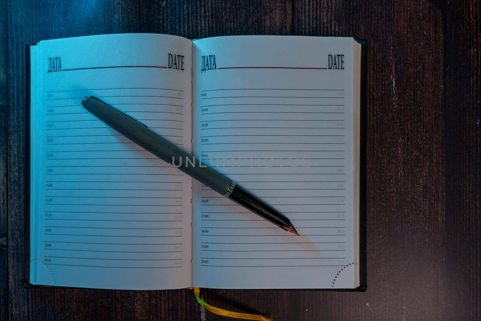 An open planner with lined pages and a fountain pen resting on it, placed on a wooden surface with dim, moody lighting. A concept of journaling, planning, and reflection