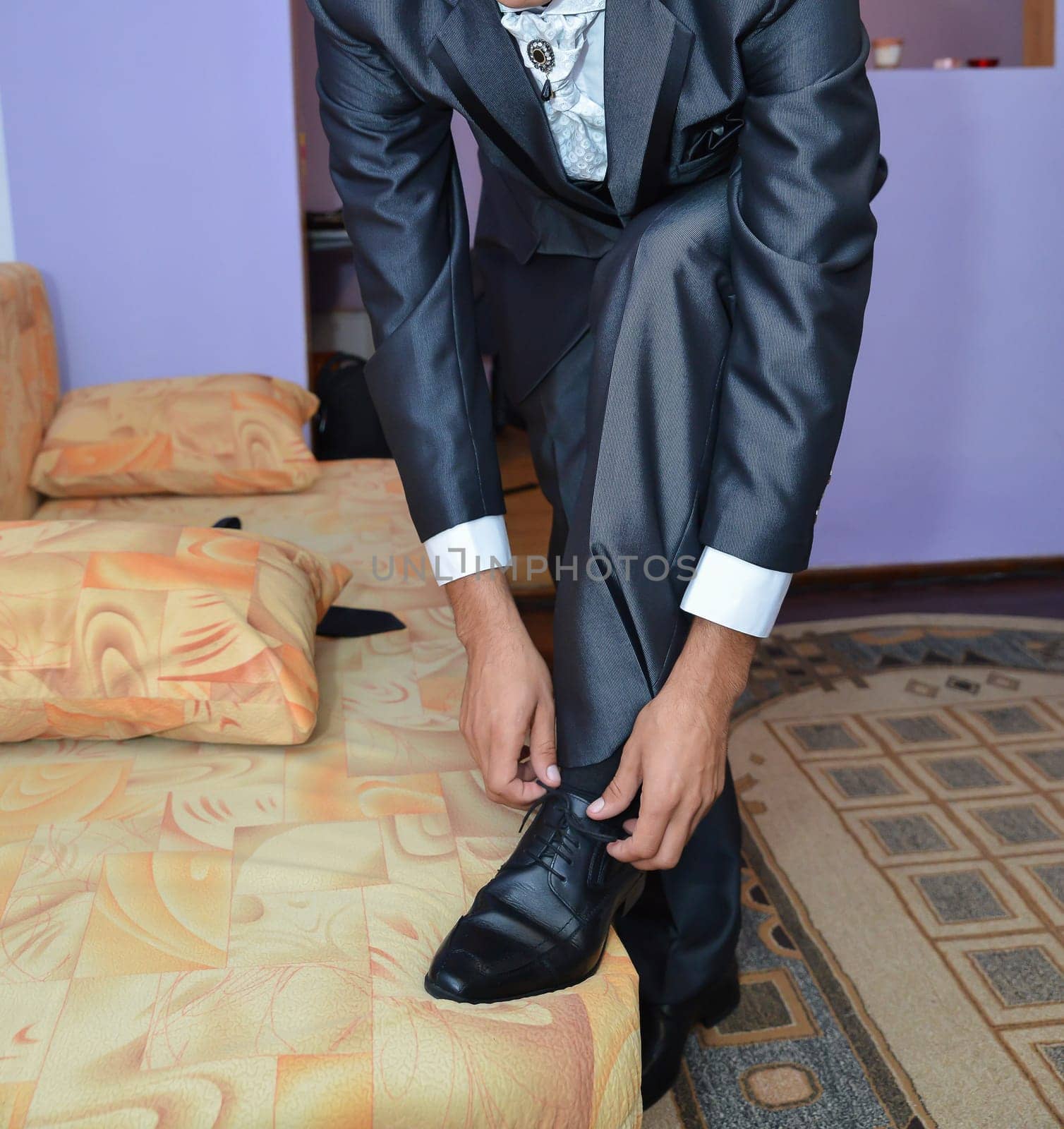 A well-dressed gentleman ties his sleek black shoes, adding the finishing touch to his elegant ensemble before stepping out in style.