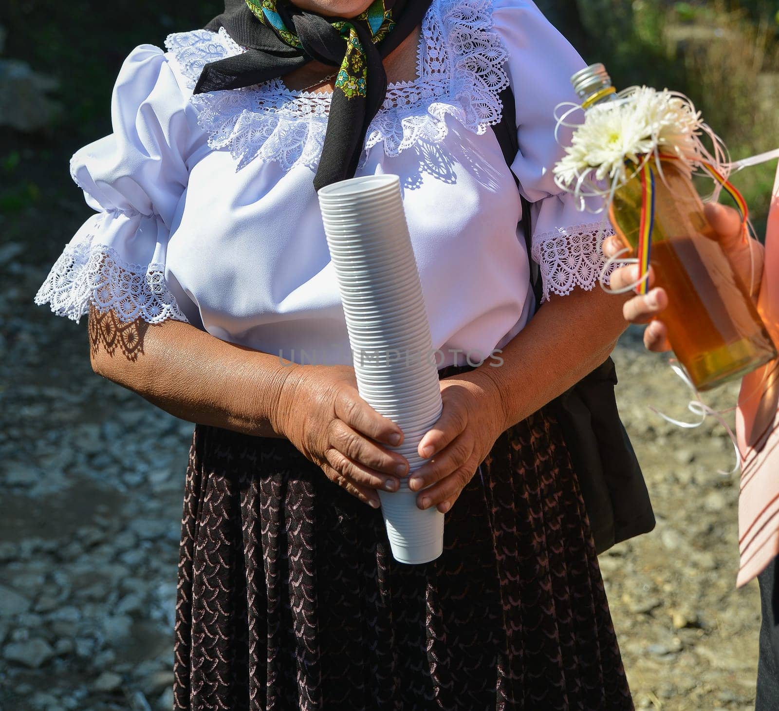 Woman in traditional clothing holds paper and bottle.
