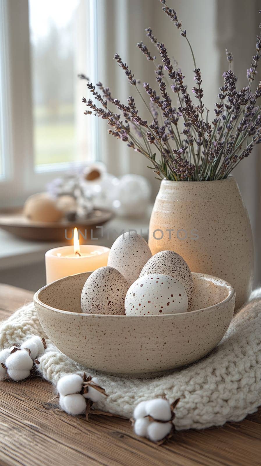 A serene indoor arrangement showcases speckled eggs nestled in a neutral bowl, accompanied by a lit candle and dried lavender, creating a cozy spring atmosphere.