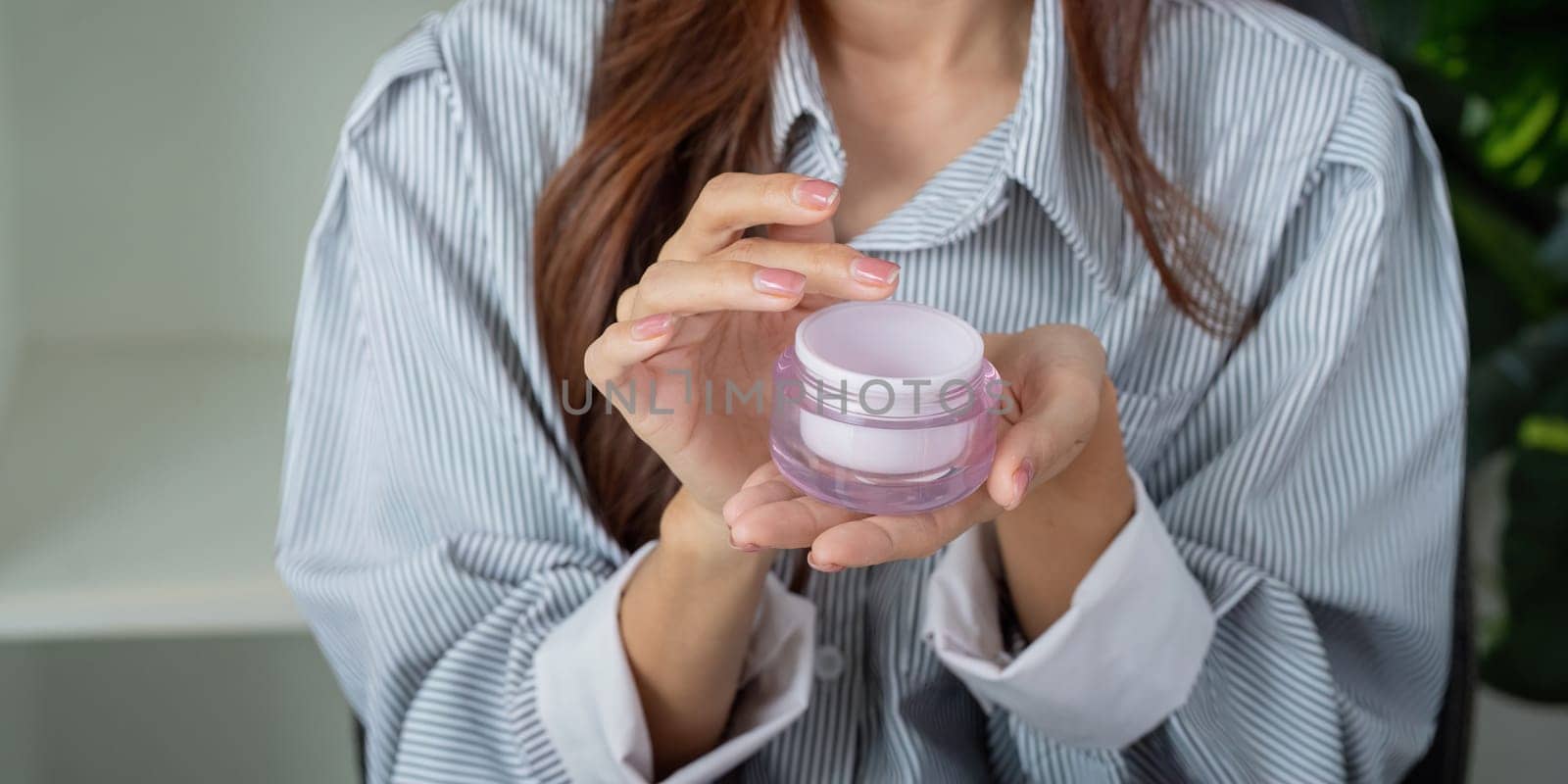 A woman showcases her favorite moisturizer in a modern and stylish setting, emphasizing self-care and skincare.