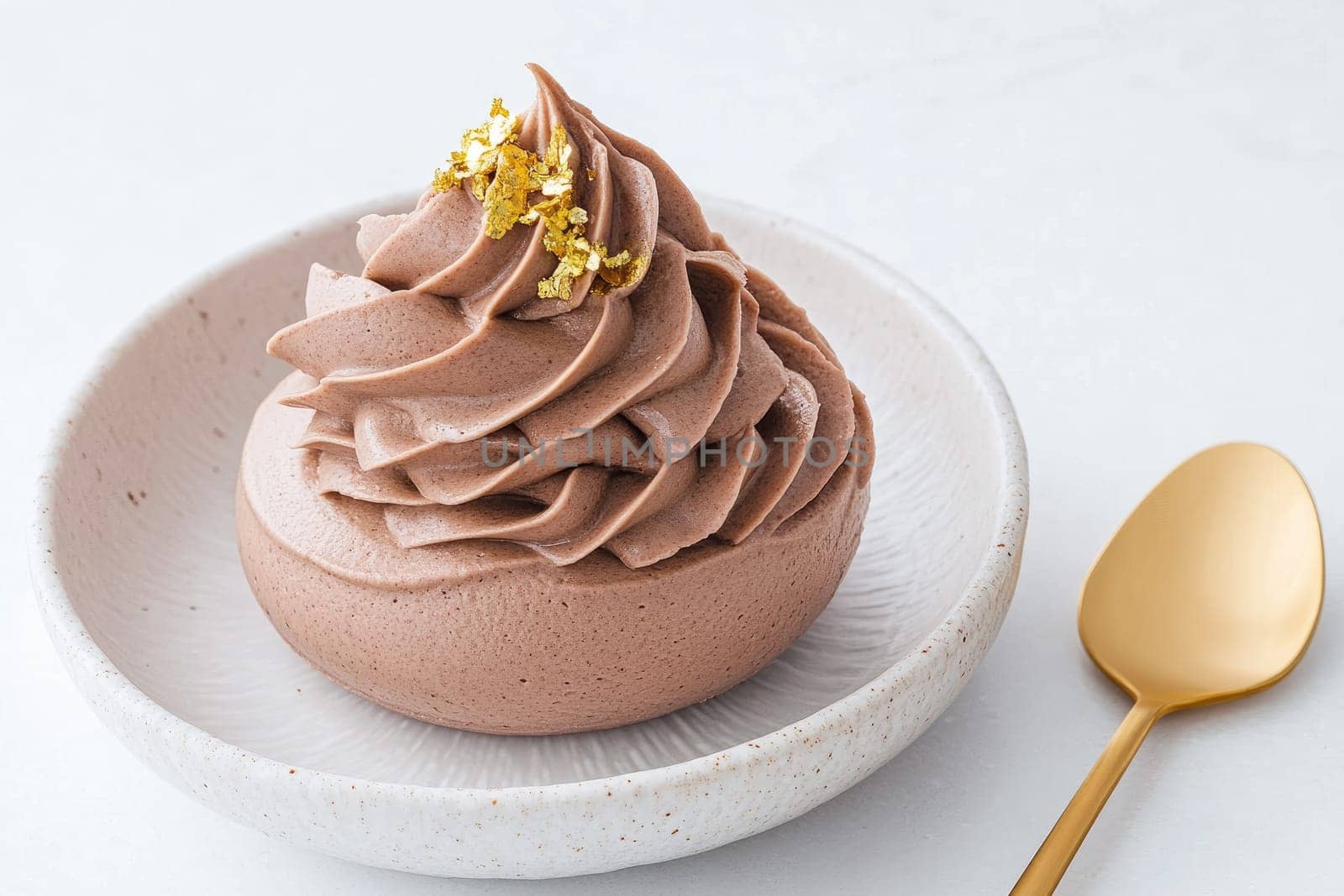 A rich chocolate mousse sits elegantly in a white ceramic bowl, adorned with delicate gold flakes, inviting a sweet and luxurious indulgence, perfect for dessert lovers.