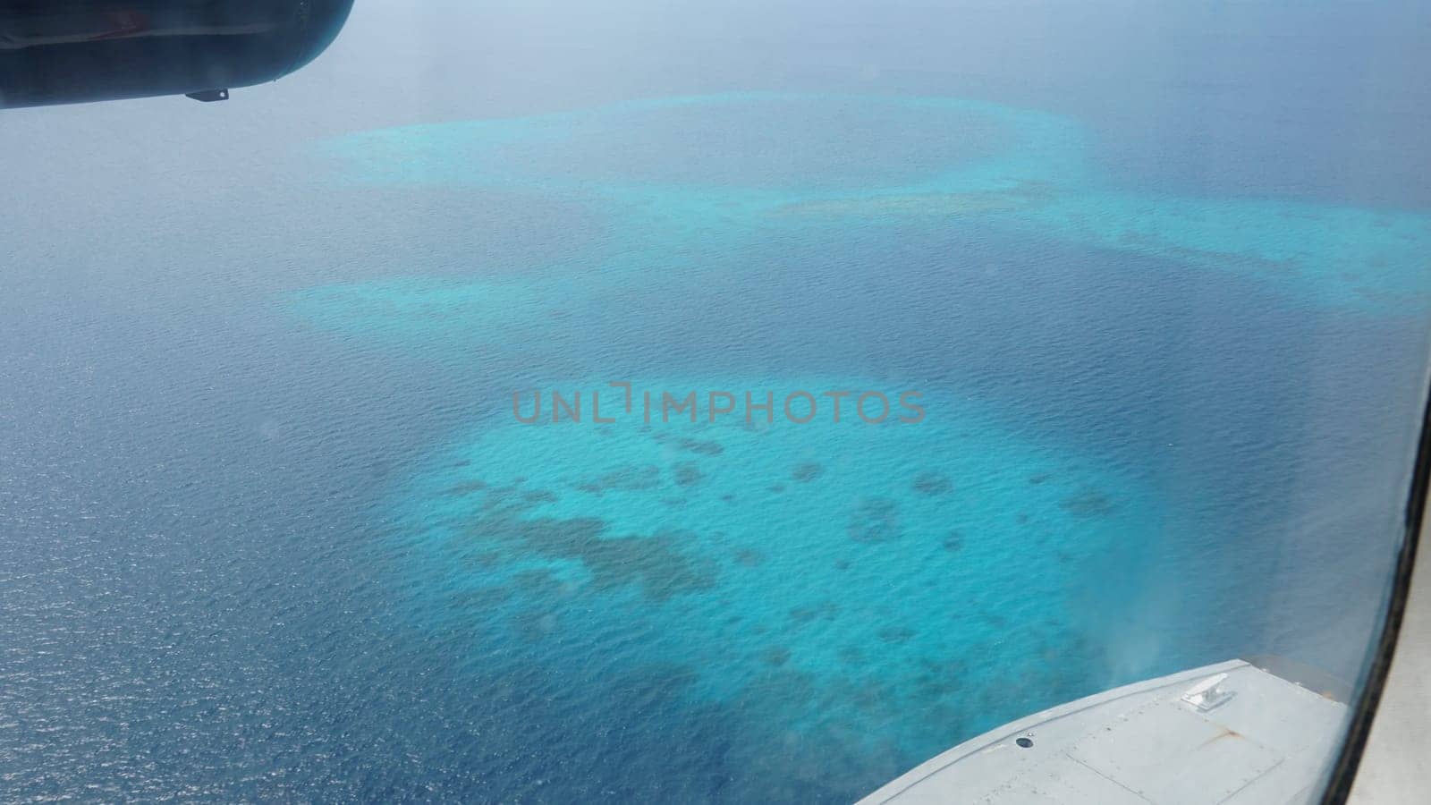 Aerial view of crystal-clear turquoise waters surrounding the coral reefs of the maldives, seen from an airplane window, showcasing the beauty of this tropical paradise