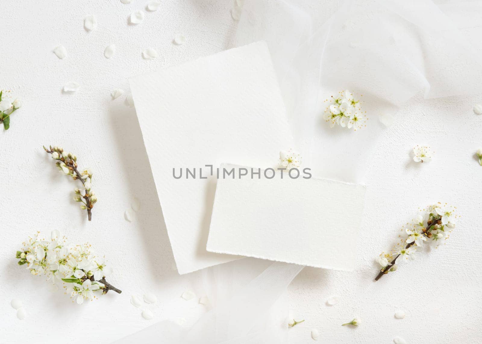 Blank cards near tulle and wild plums white flowers top view, mockup. Pastel cards for spring party design or romantic wedding stationery. Close to nature or mothers day concept