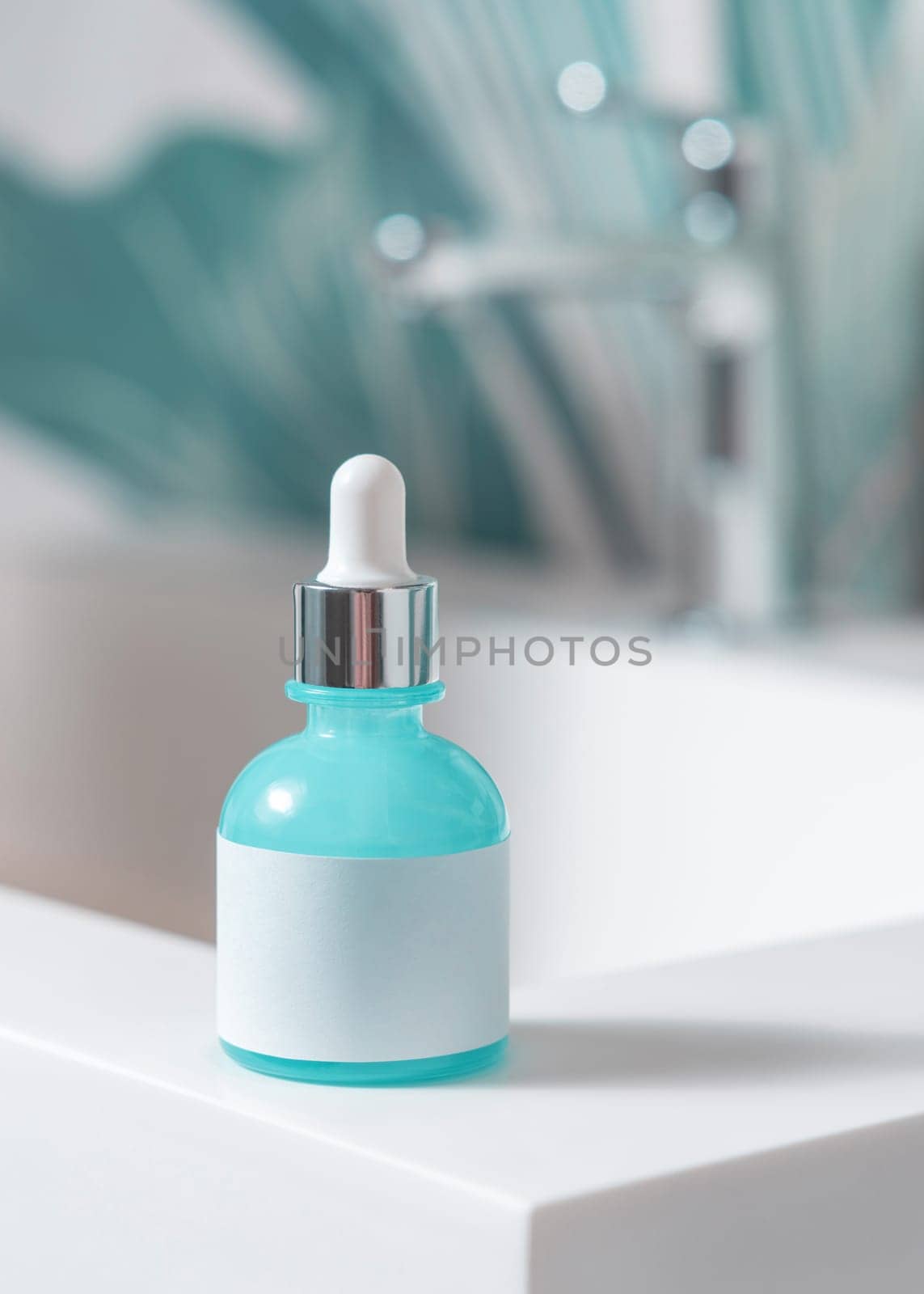 Blue glass dropper bottle with pipette and blank label on washbasin with faucet in green tropical bathroom close up. Natural cosmetics - serum or essence. Daily beauty procedures