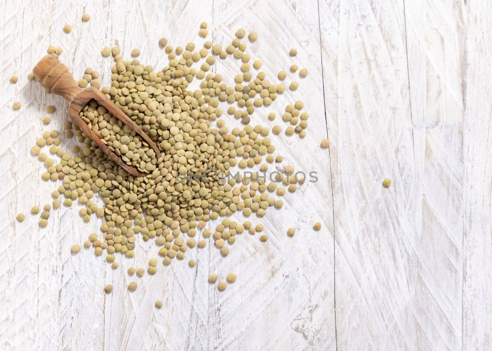 Wooden scoop full of dried green lentils on white table top view, copy space. Healthy vegetarian food, legumes plant-based protein source. Traditional mediterranean raw uncooked cousin ingredient