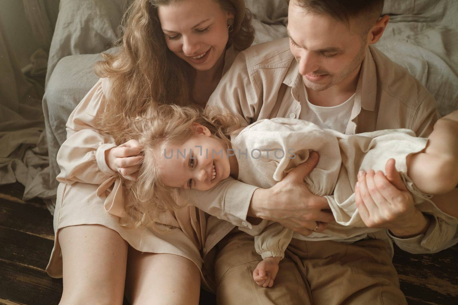 A family shares a joyful moment in a cozy room, with a child playfully lifted by a parent while the other parent watches, creating a warm atmosphere filled with laughter and love.