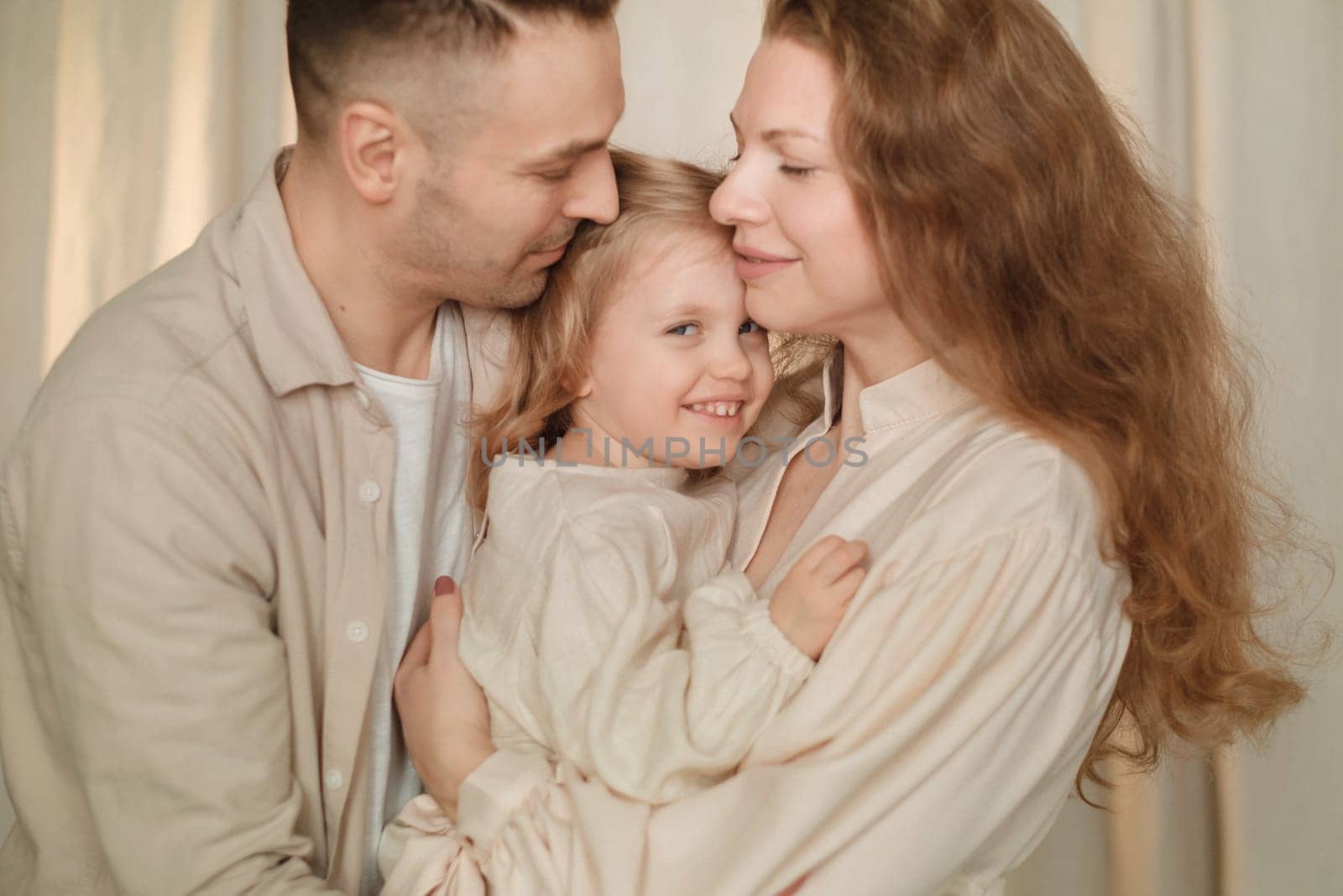 Parents share a tender moment with their smiling child in a soft-lit living room. The atmosphere is filled with warmth and love as they enjoy each other's company.