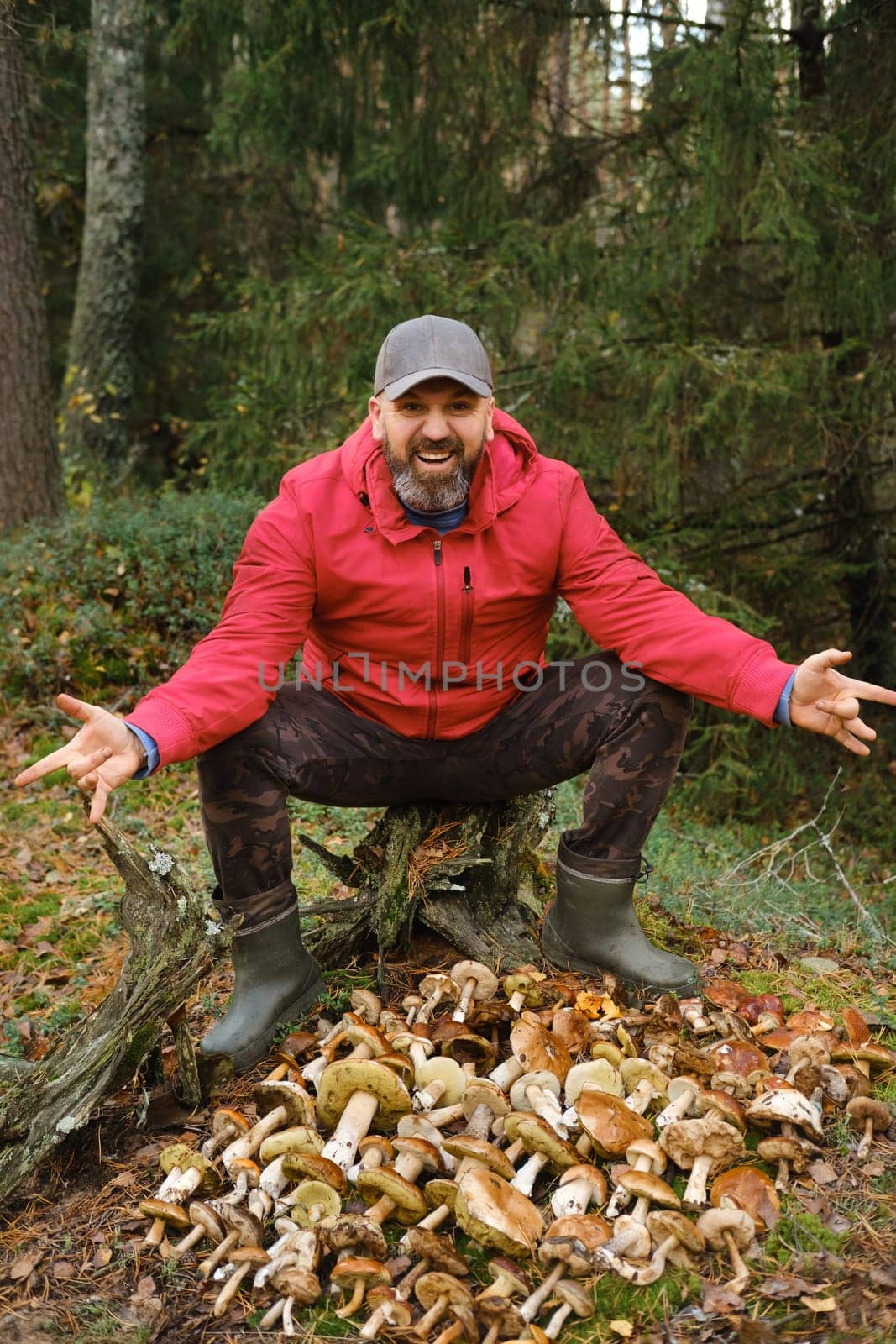 A happy forager proudly displays a large collection of various mushrooms in a lush green forest, enjoying the beautiful autumn day surrounded by trees and foliage.