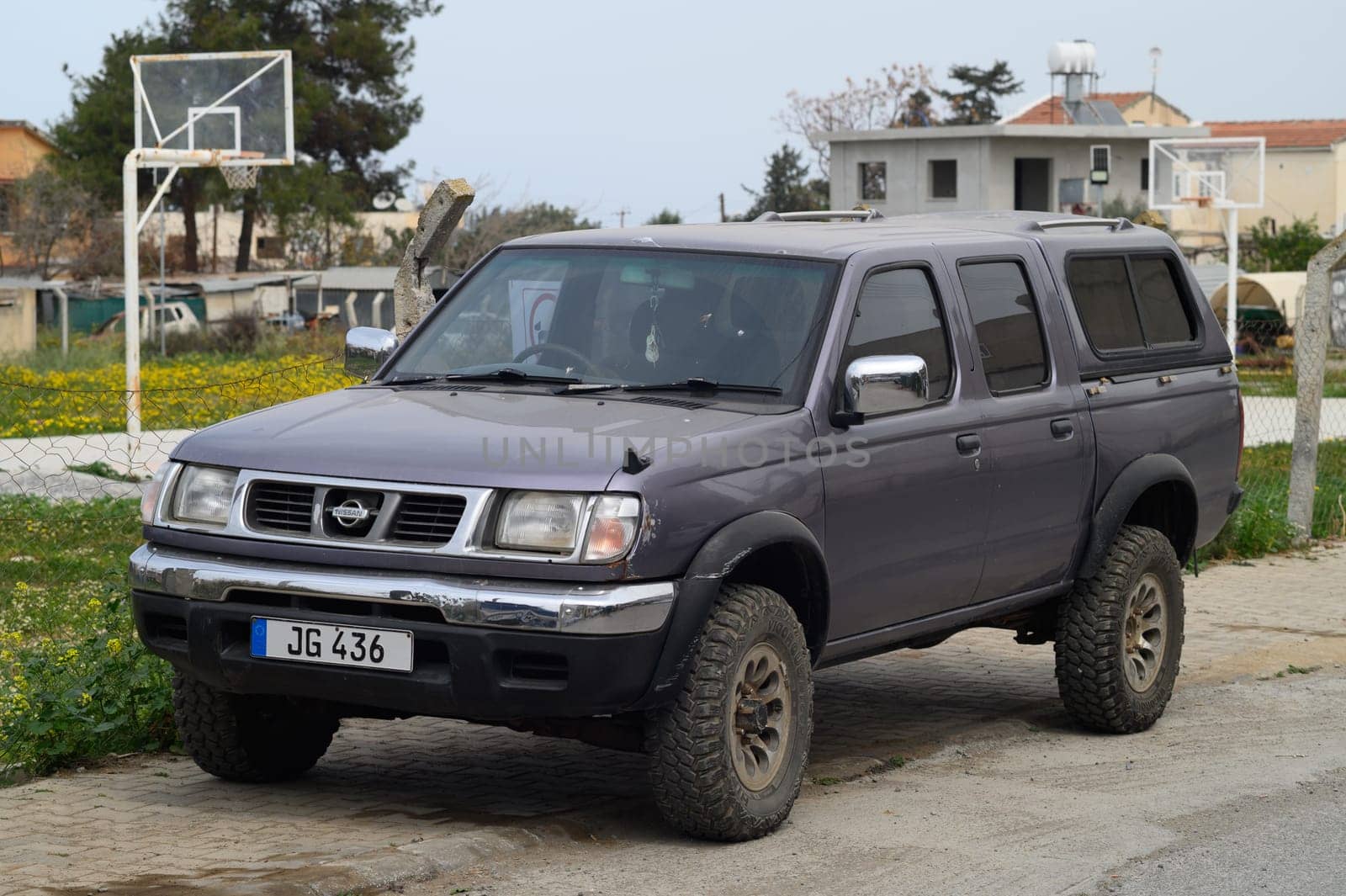 Gaziveren Cyprus -17.03.2025 A rugged Nissan Patrul pickup truck parked on a gravel road, surrounded by vibrant wildflowers. Nearby, residential homes stand under a clear blue sky, creating a tranquil atmosphere perfect for exploration.
