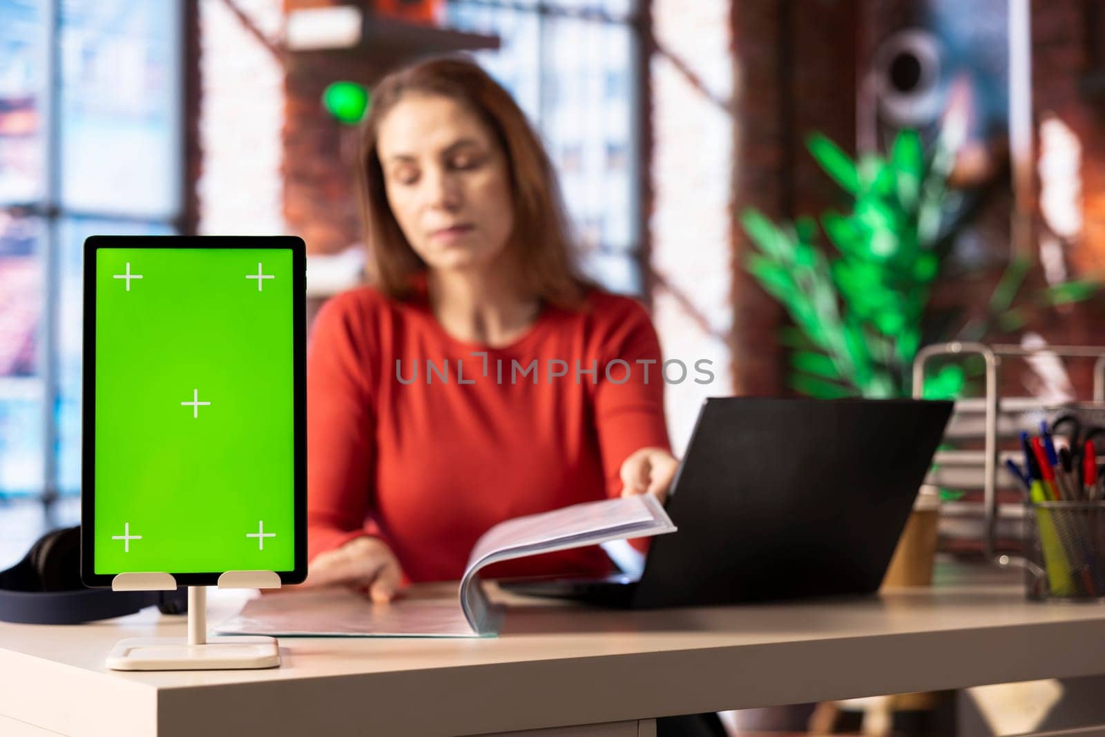 Person at her home office reading news and research papers with green screen, virtual connection online. Woman collecting notes and data from different sources to know current events.