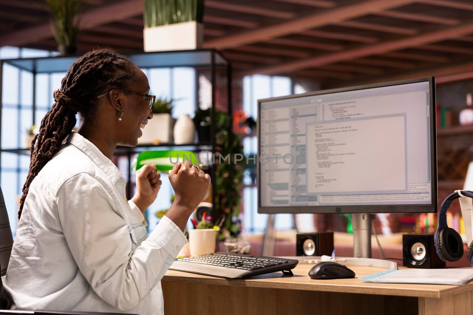 Happy programmer in home office celebrating after successfully executing programming code, looking at UI on computer monitor. Joyous IT worker satisfied after testing code and seeing good results