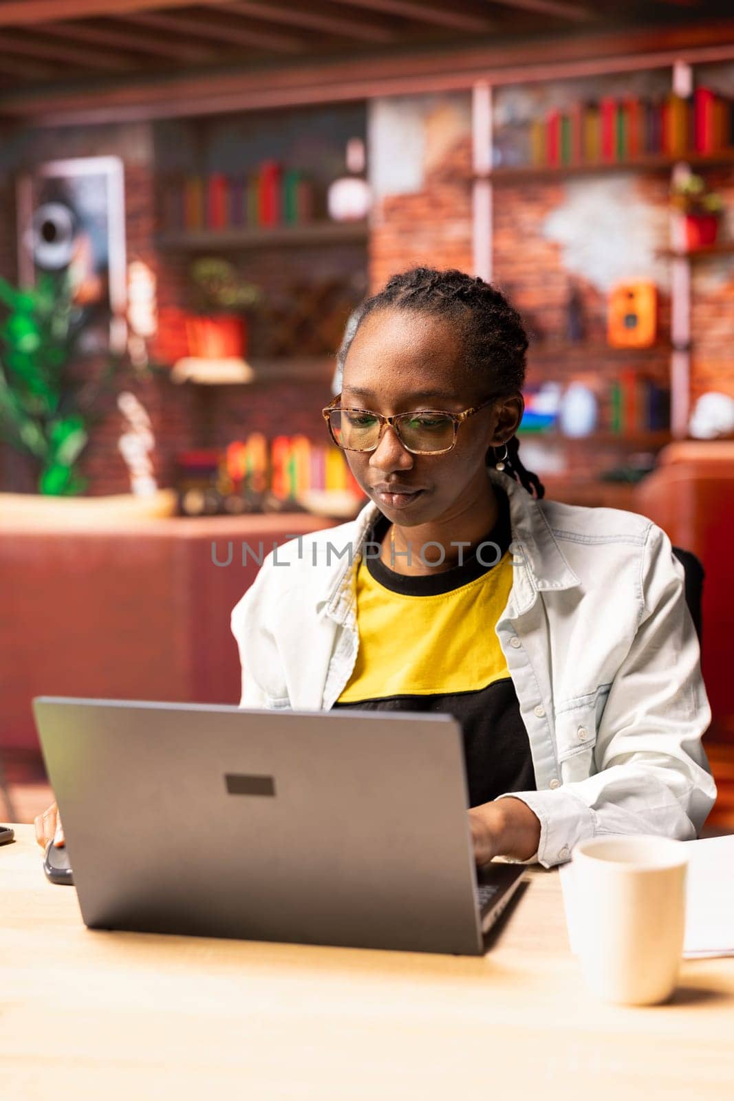 Freelancer in home office using laptop device to work on job tasks. African american remote employee using notebook to do customers relations job online, answering inquiries