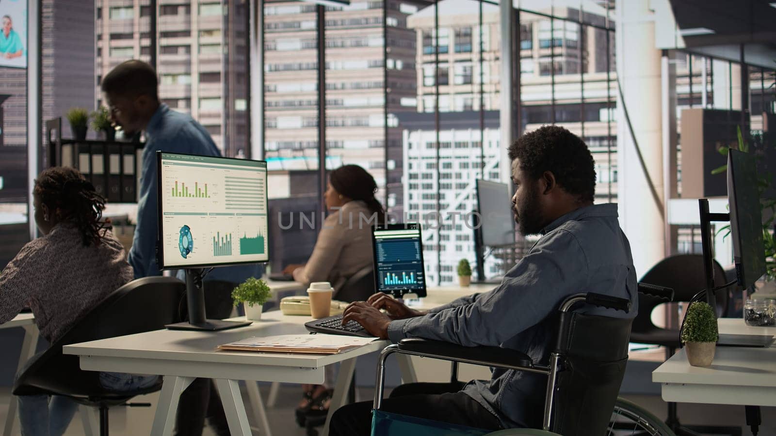 African american male worker in wheelchair trying to solve daily tasks at the office, examining organizational data and working on a forecasting plan. Man with impairment ensures analysis. Camera B.