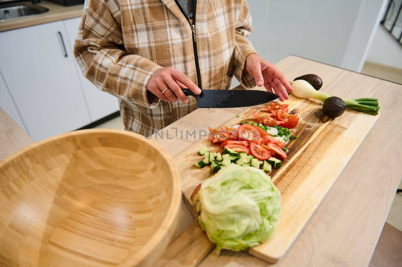 A person is seen chopping fresh vegetables on a wooden cutting board to prepare a healthy salad. Nearby, a large wooden salad bowl and additional vegetables are visible in the kitchen setting.