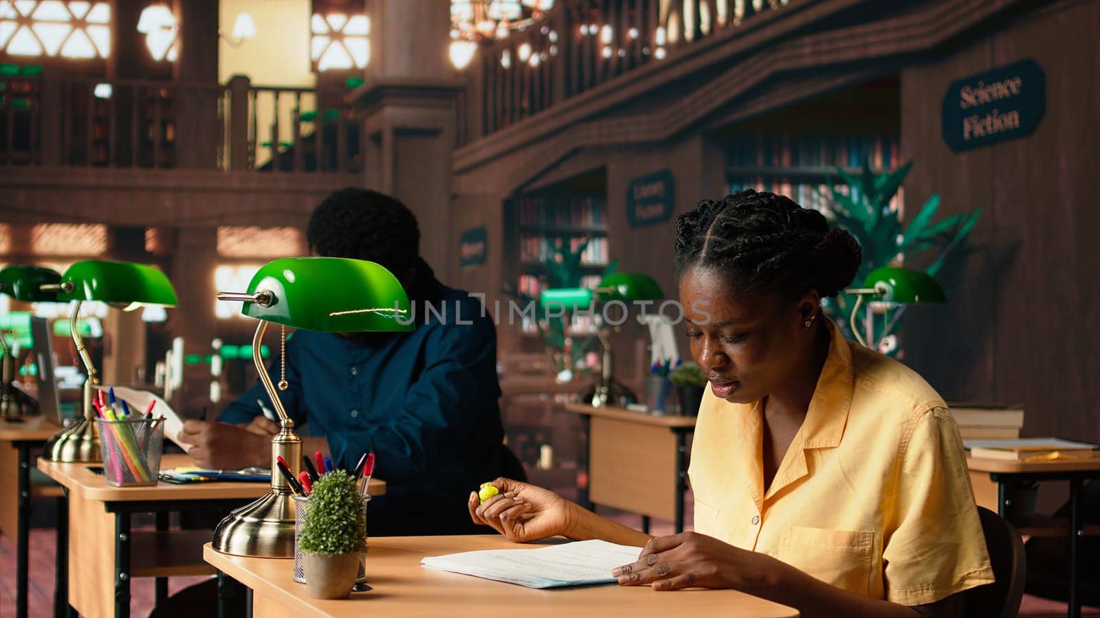 African american pupil highlighting key words from the class notes, creating a summary to study easily and memorize the lesson theory. Student using a learning technique in the library. Camera A.