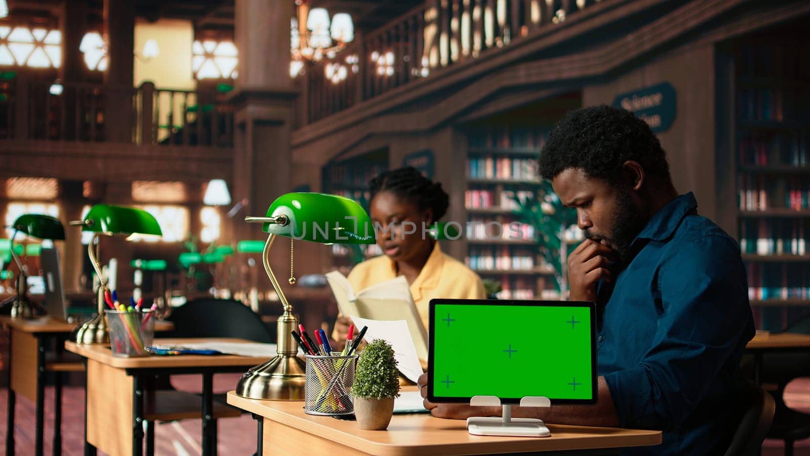 African american students consulting research papers next to green screen from the academic database, learning information from copy books. Young team of pupils at the library. Camera A.