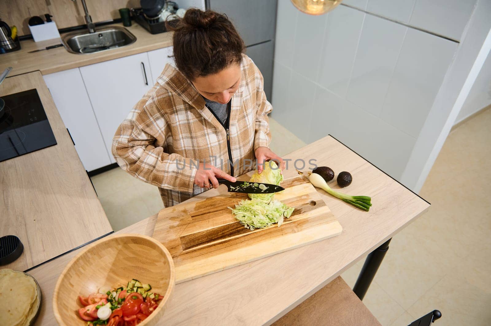 Person slicing vegetables on a cutting board in a well-lit modern kitchen. The scene showcases fresh produce, a warm atmosphere, and the theme of healthy living and home-cooked meals.