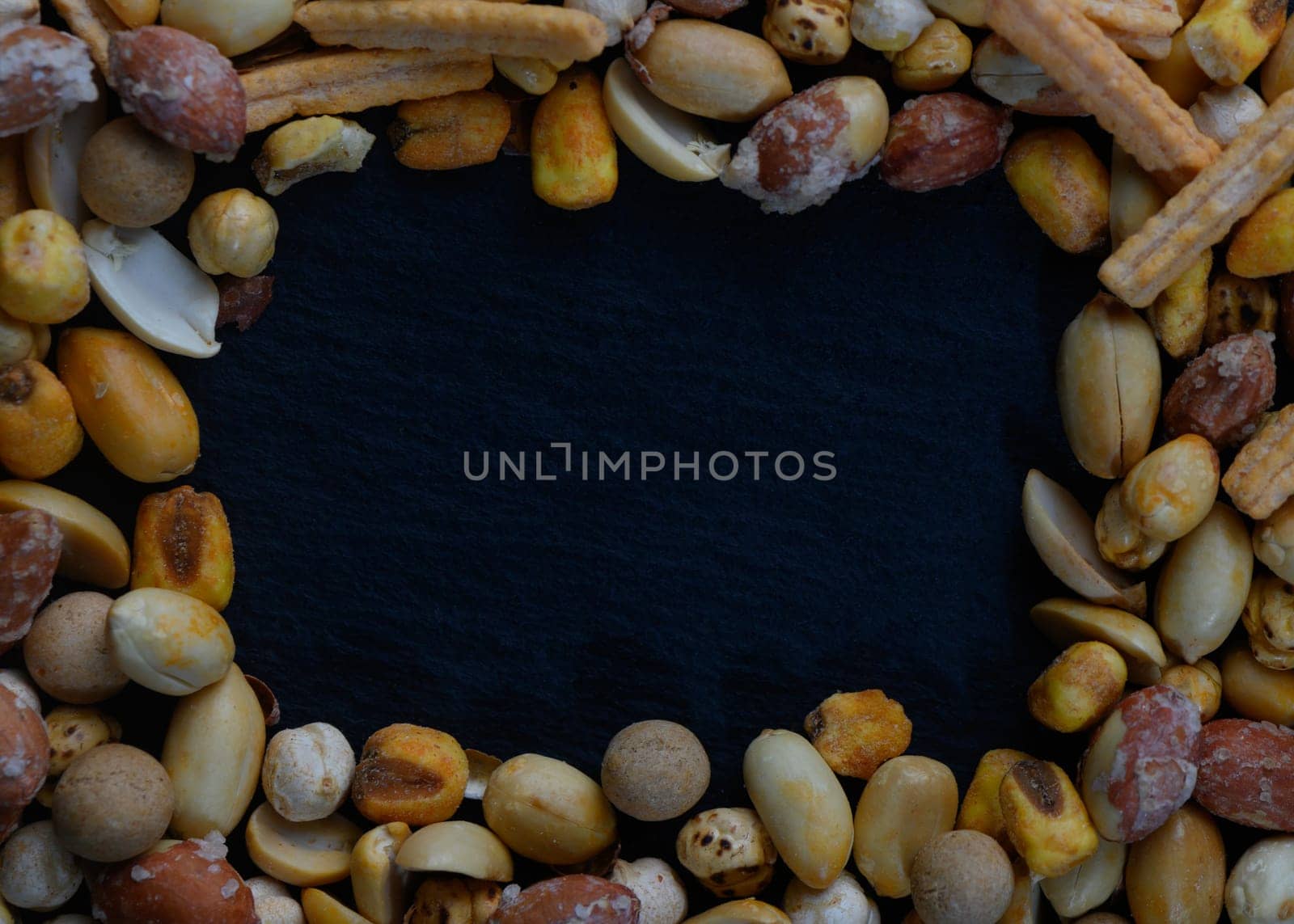 A vibrant array of mixed nuts and savory snacks beautifully frames a dark background, ideal for showcasing delicious recipes or gourmet culinary delights.