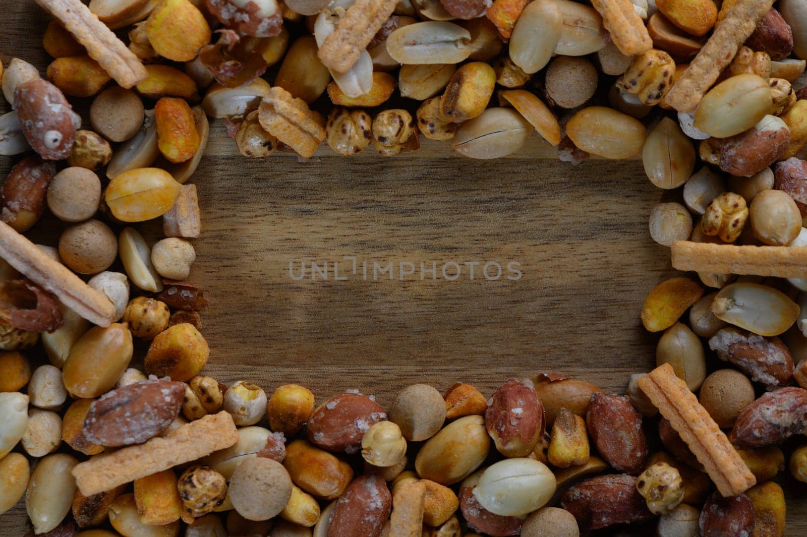 A vibrant array of nuts and savory snacks arranged beautifully around a wooden surface, perfect for sharing or as a delightful centerpiece during gatherings.