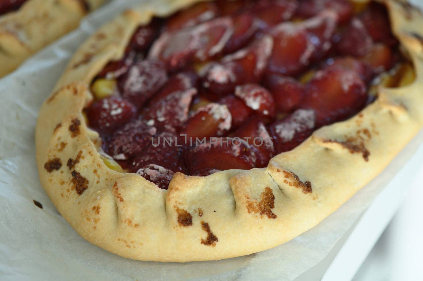 A freshly baked cherry galette rests on parchment paper, showcasing its golden crust and glossy fruit filling. The warmth and aroma fill the cozy kitchen, enticing everyone nearby.