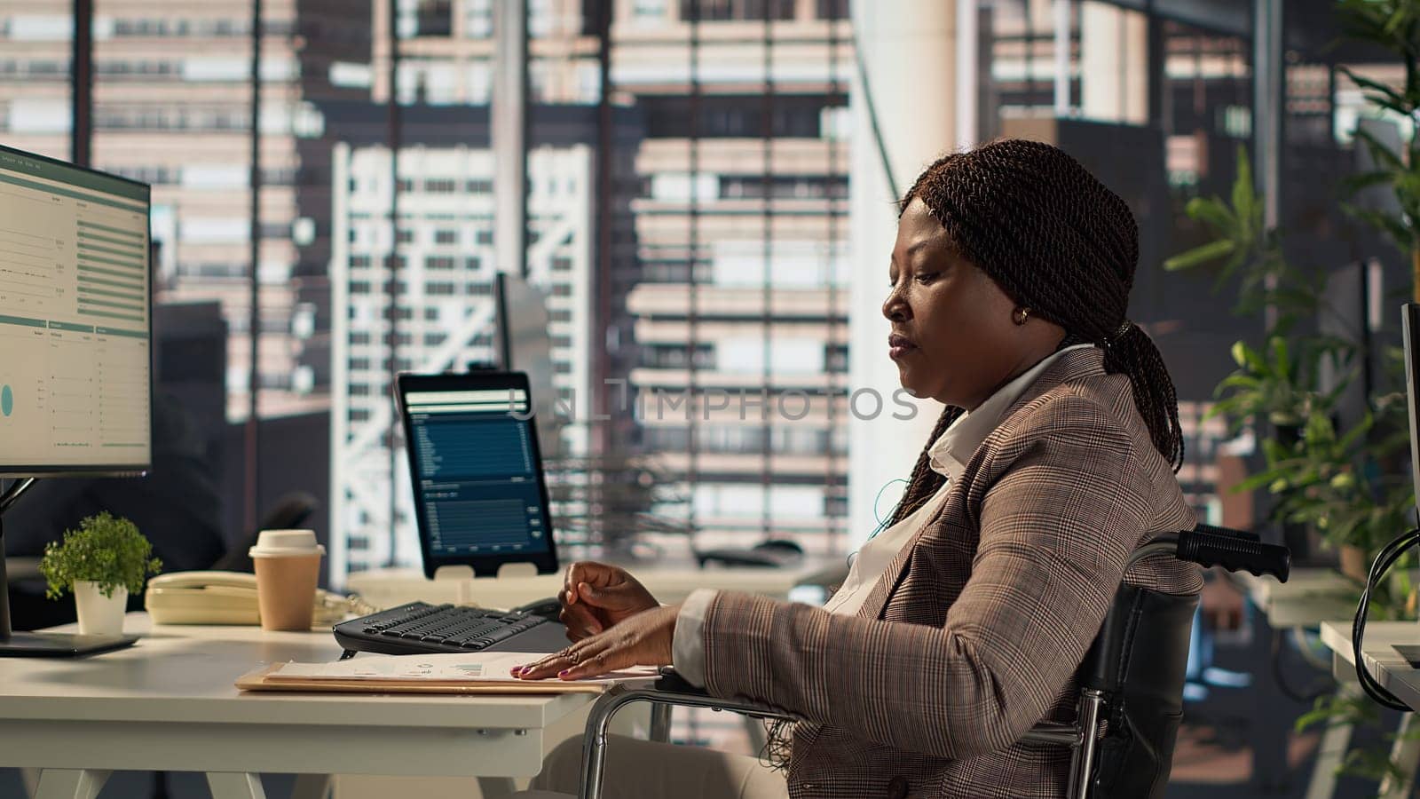 Female boss with chronic disability examining archived files and data reports, creating a financial plan before allocating resources. Businesswoman in wheelchair review infographics. Camera A.