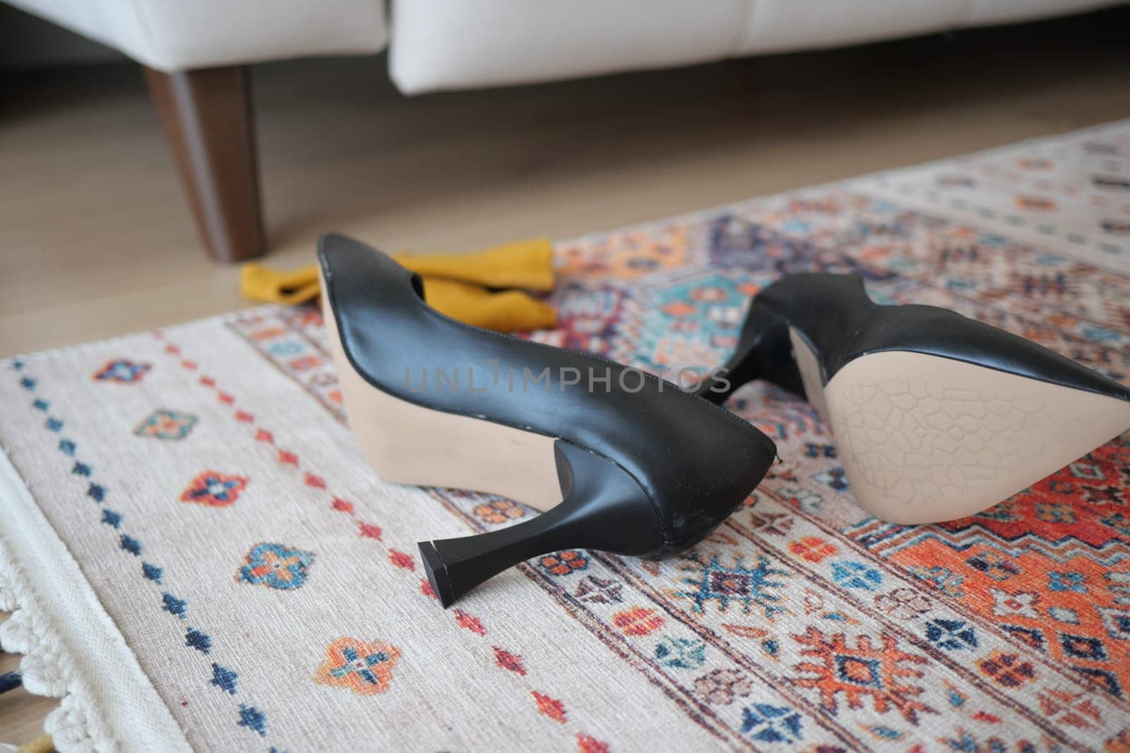 Two black high heels resting on a decorative rug in a cozy setting.