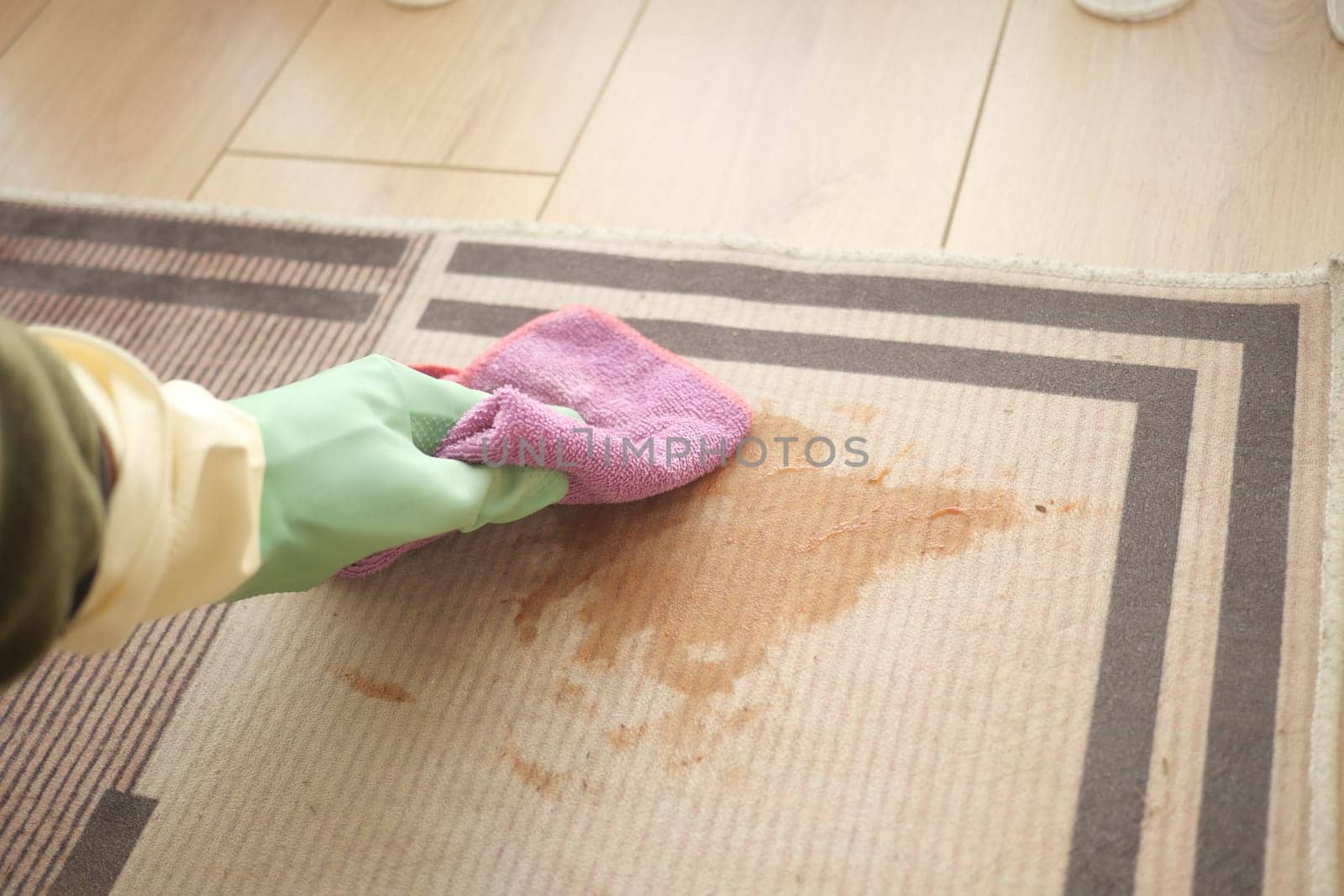 A person is scrubbing a stained carpet using a cloth while wearing gloves.