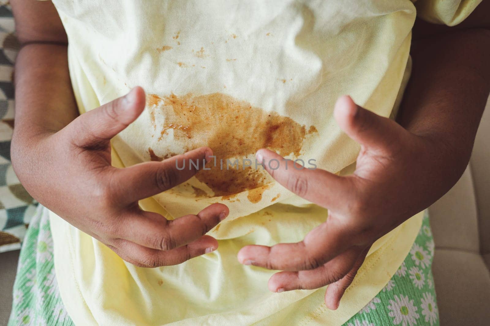 A child sits with hands on stomach, showing a stained yellow shirt.