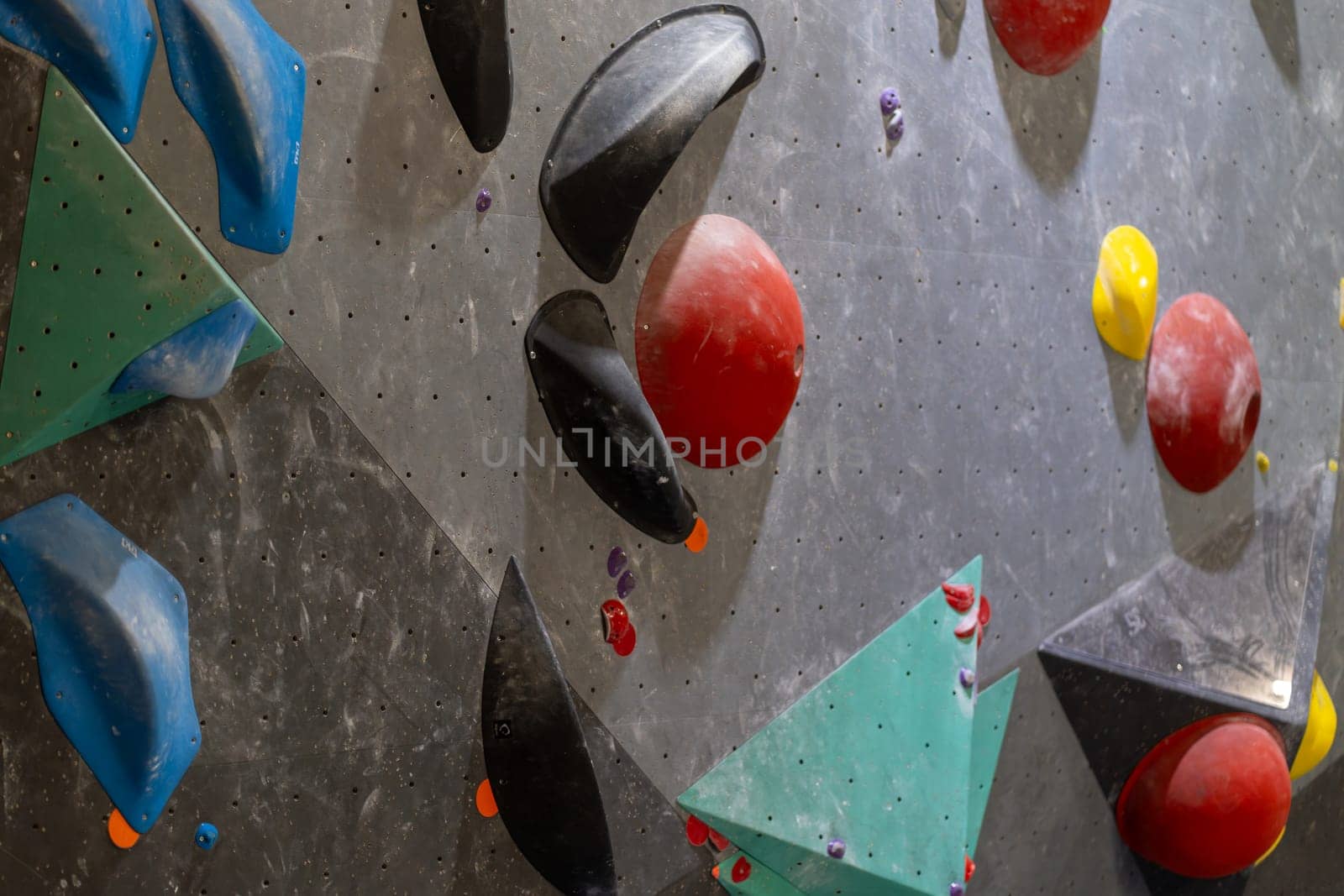 Colorful climbing holds on gray gym wall, showcasing a full frame of an artificial rock climbing wall with various handles for climbing in closeup
