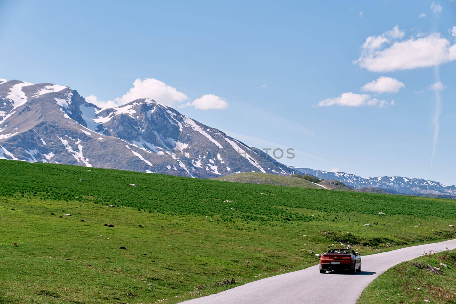 Red convertible is driving along a road in a green mountain valley. Back view. High quality photo